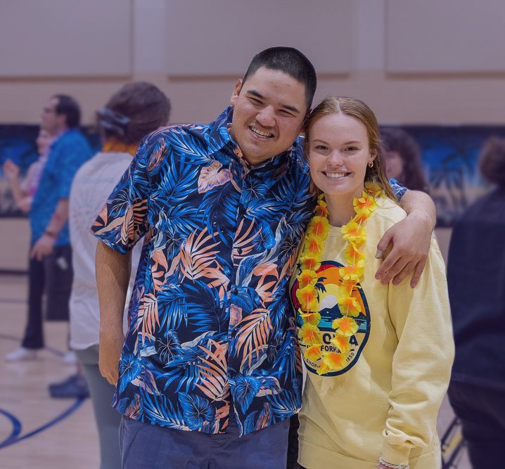 Two smiling people pose together indoors at a casual community social event.