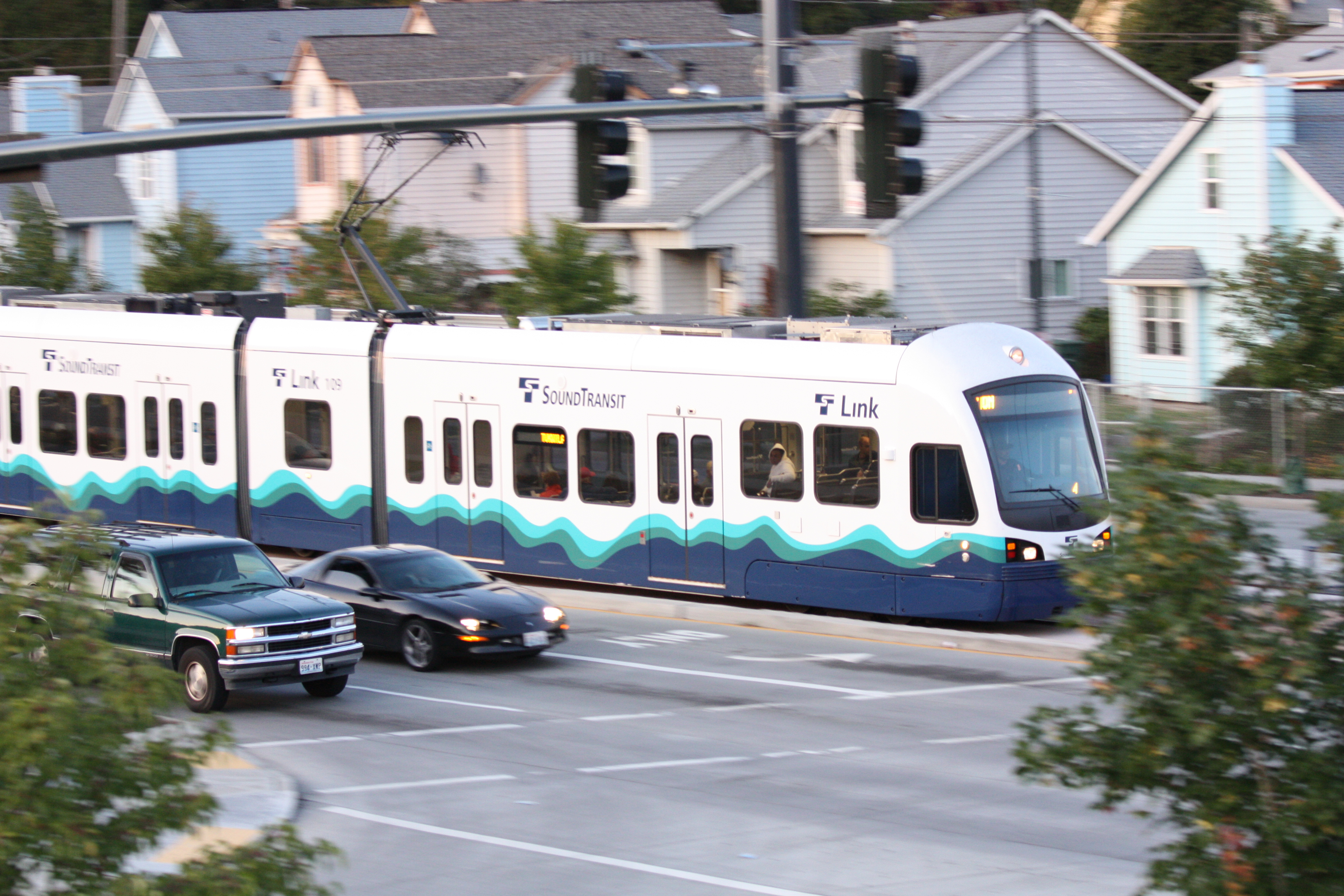 Sound Transit Link light-rail train passing through a residential street-level corridor.