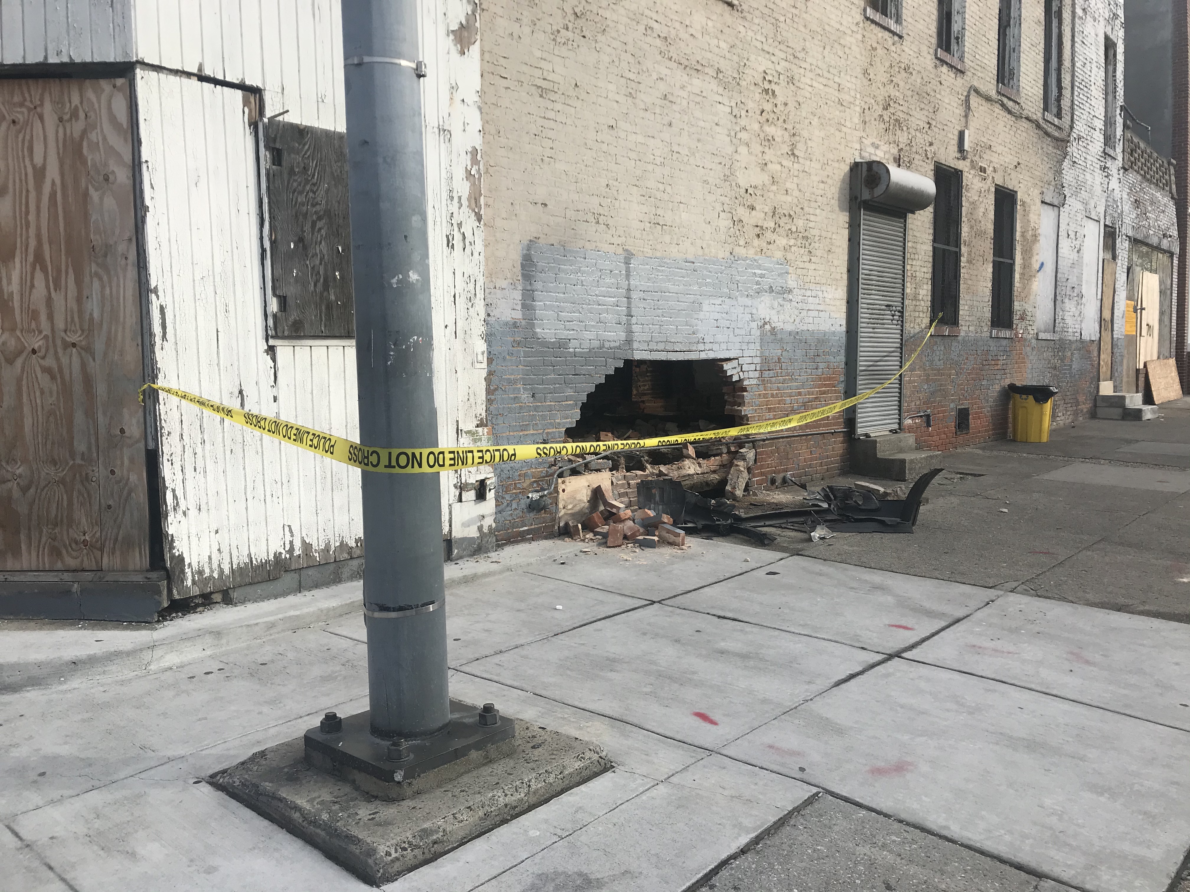 Hole in brick building wall with police tape, rubble, and a utility pole in the foreground.