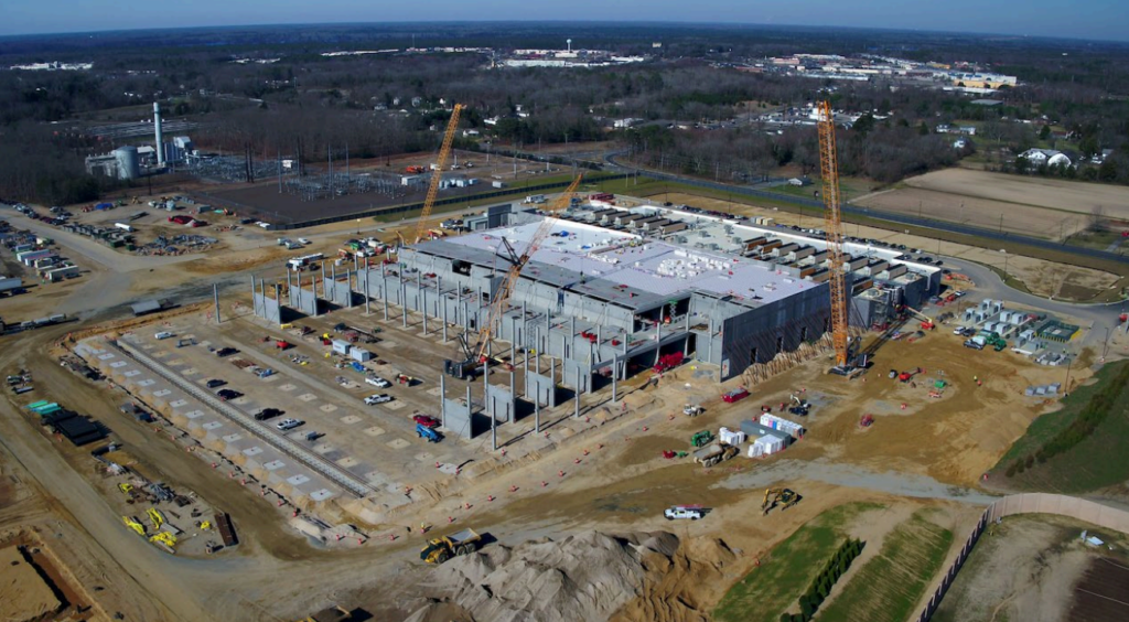Aerial view of a large building under construction with cranes and cleared land.