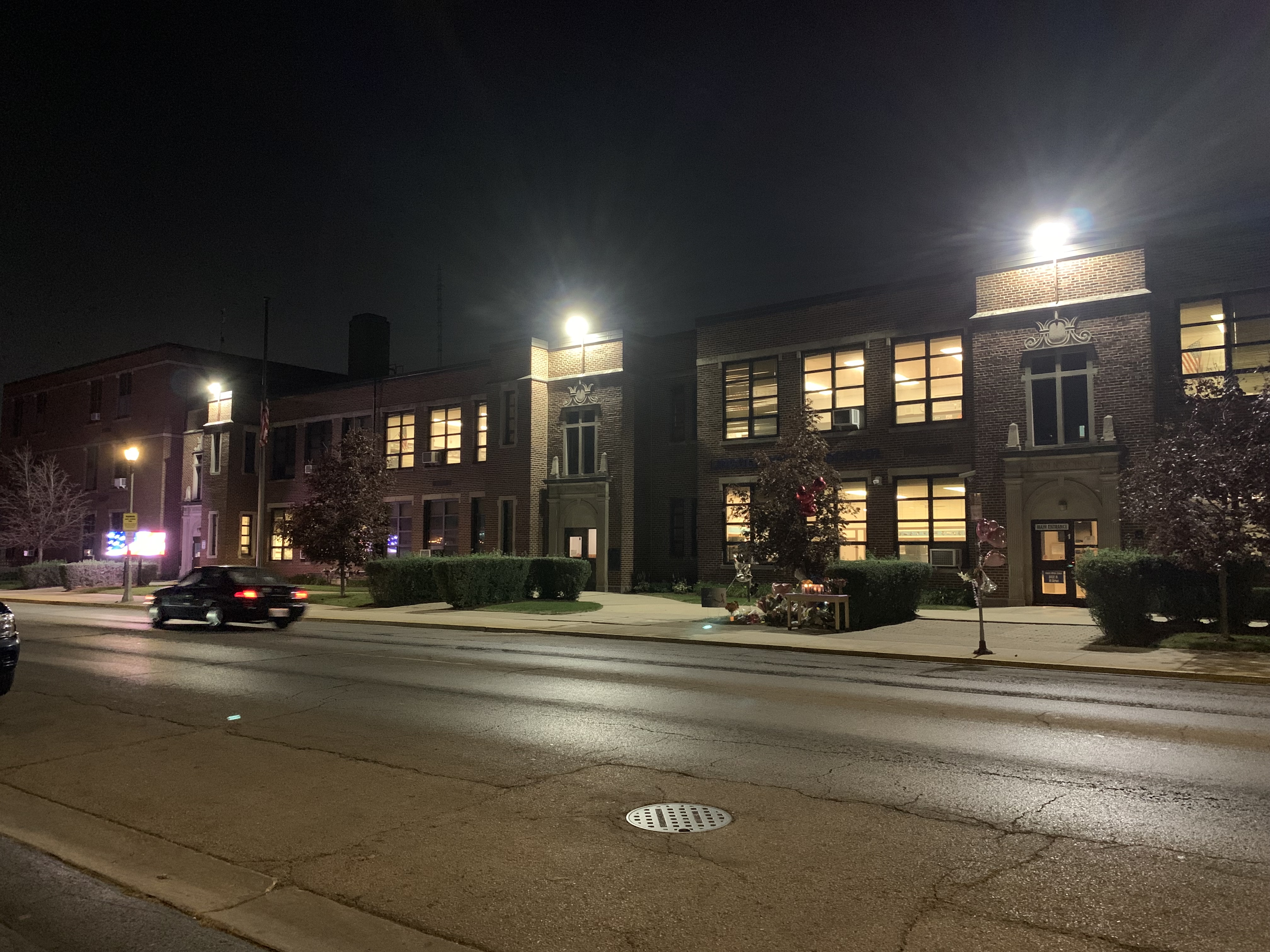 Multi-story brick school building illuminated at night with a street in the foreground.