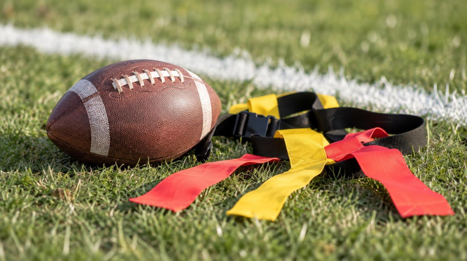 A football and flag football belts laid out on green grass near a white yard line.
