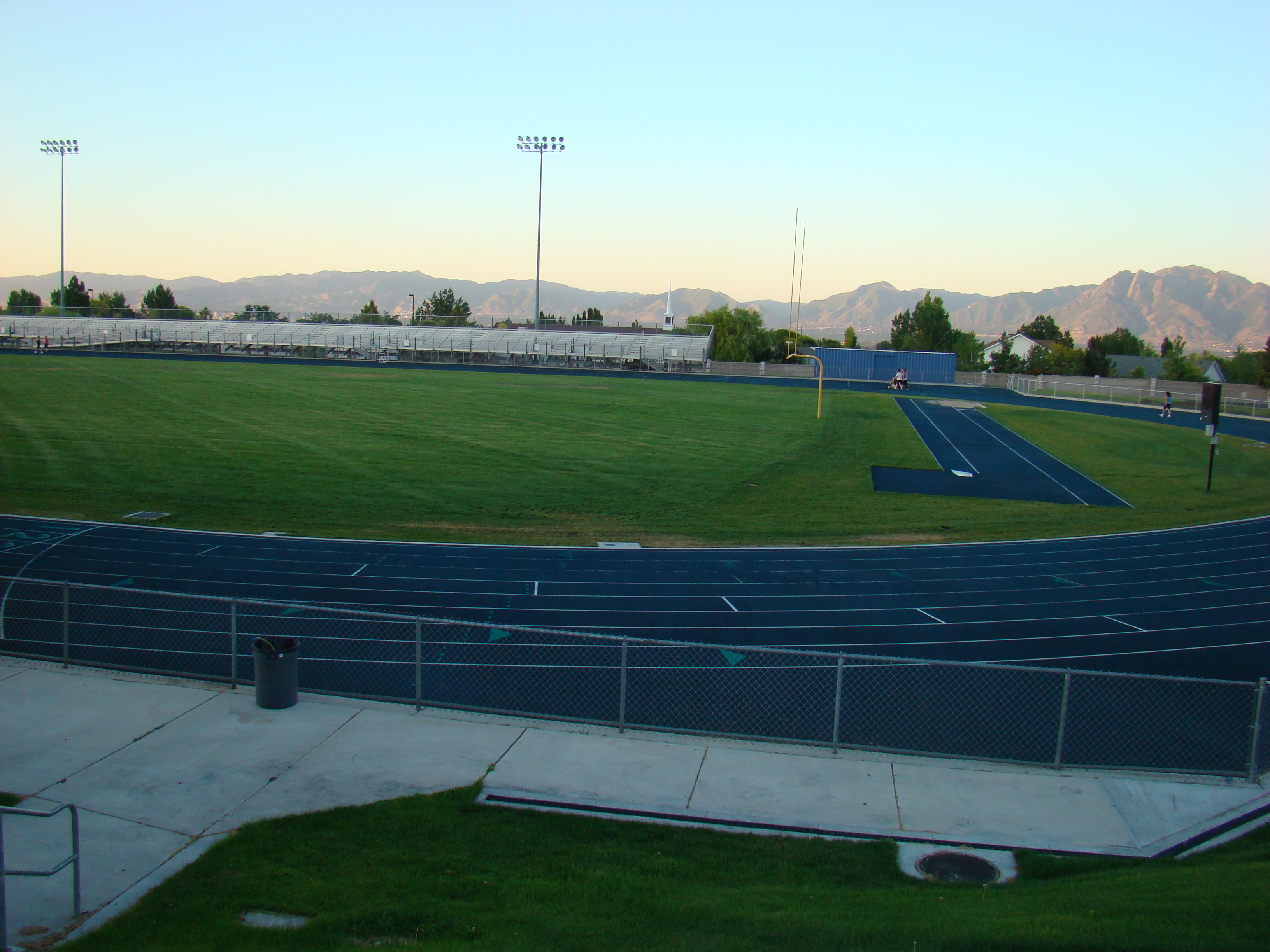 Synthetic running track and green turf football field with stadium lights and bleachers.