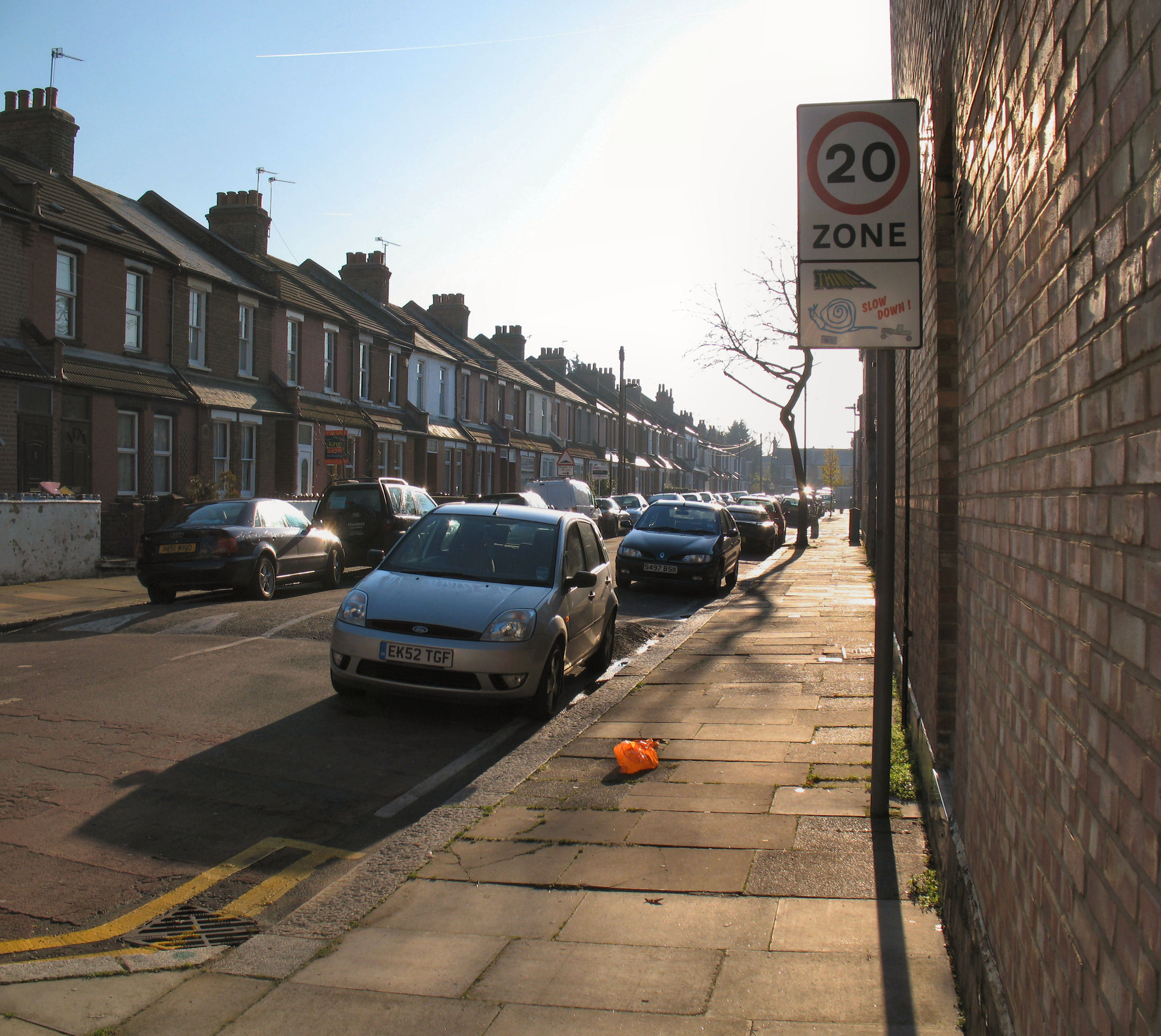 A 20 mph zone sign mounted on a brick wall beside a residential street.