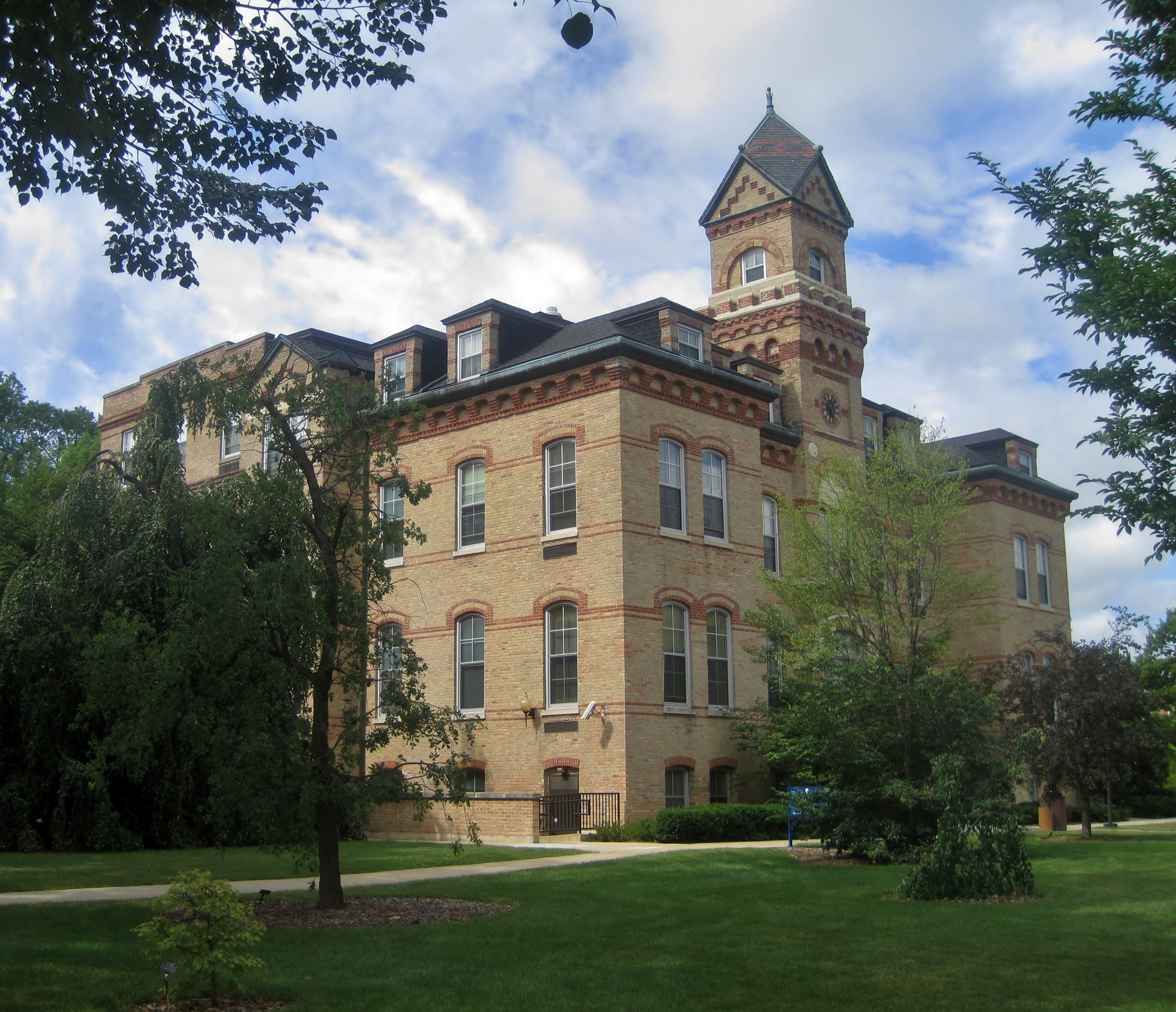 Historic brick university building with clock tower surrounded by trees.