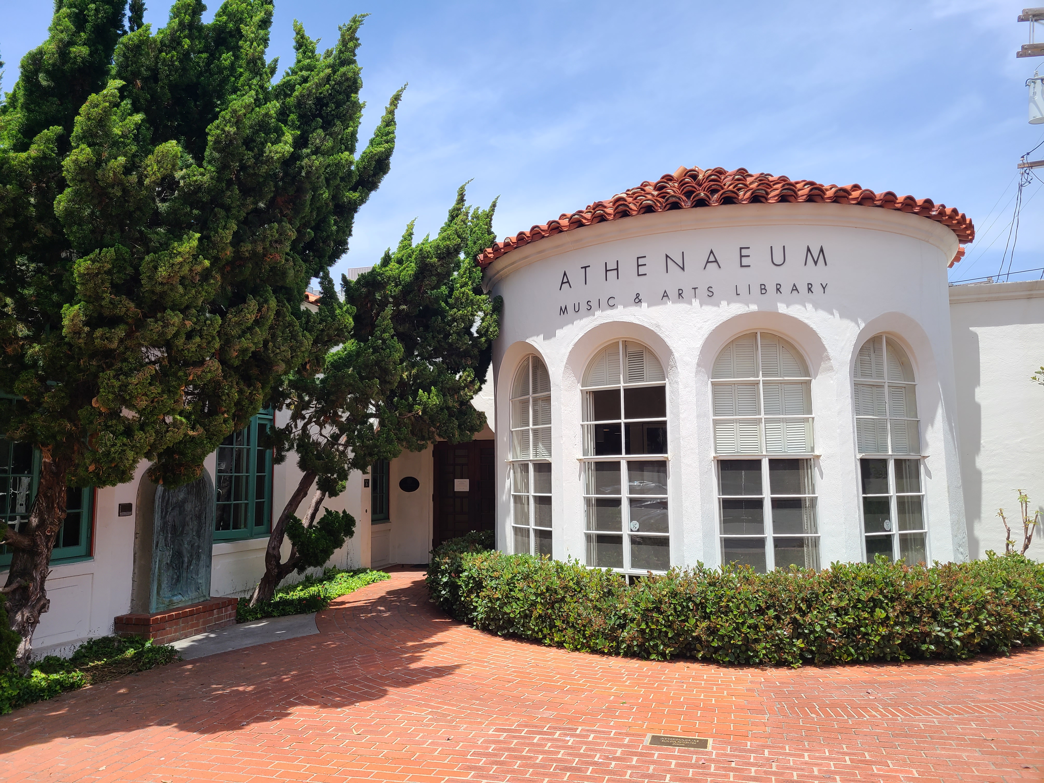 White stucco building with arched windows and red tile roof surrounded by trees.