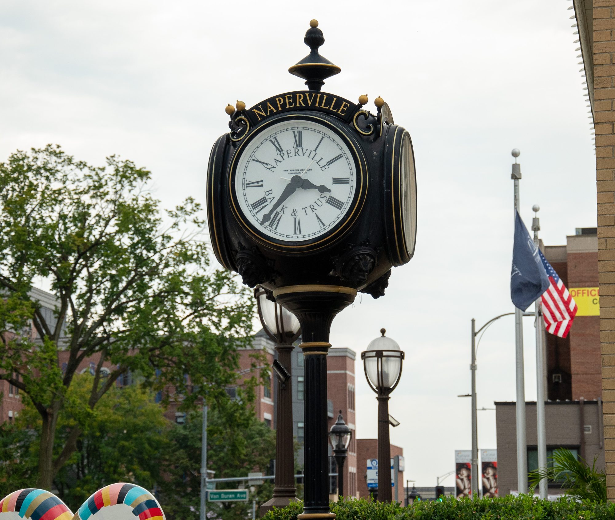 Ornate black-and-gold street clock labeled Naperville on a downtown sidewalk.