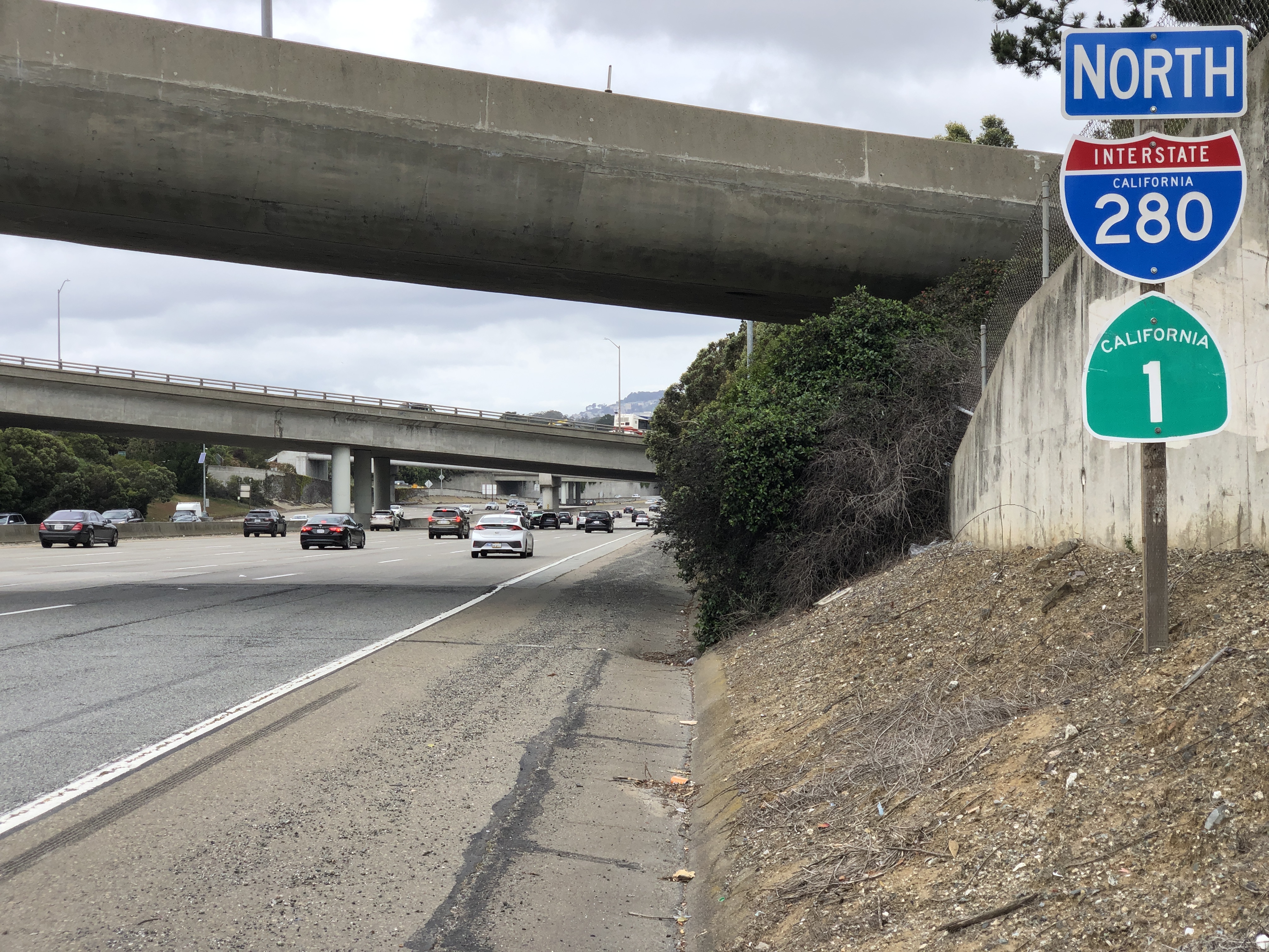 Multi-lane freeway with I-280 highway signs and an overpass in San Mateo County, California.