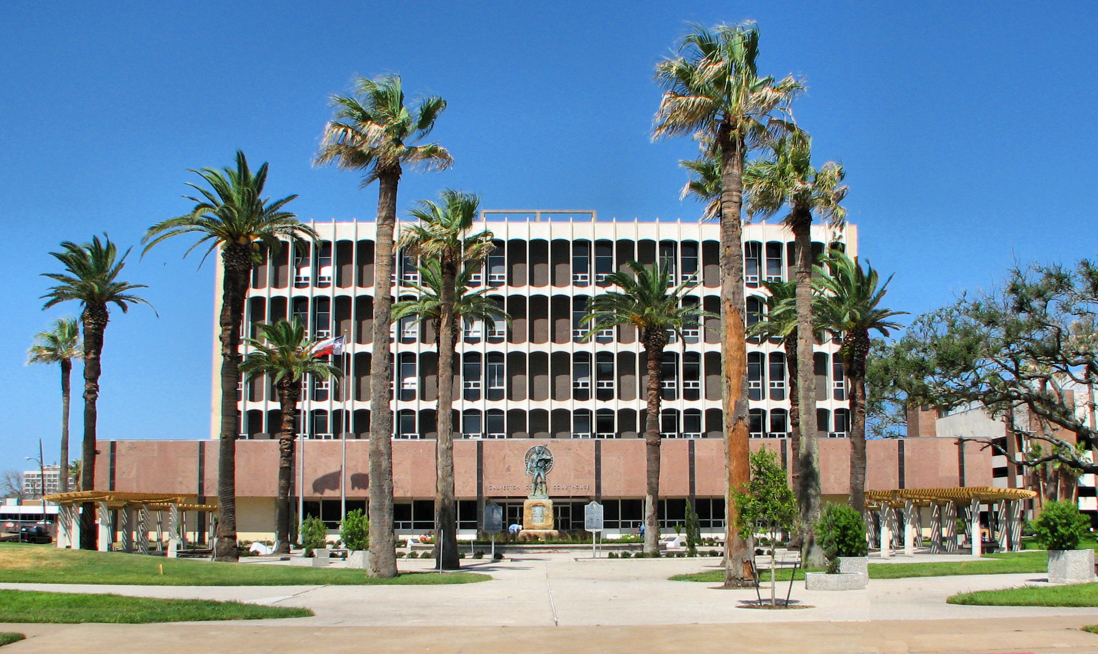 Multi-story mid-century modern government building flanked by tall palm trees under a blue sky.