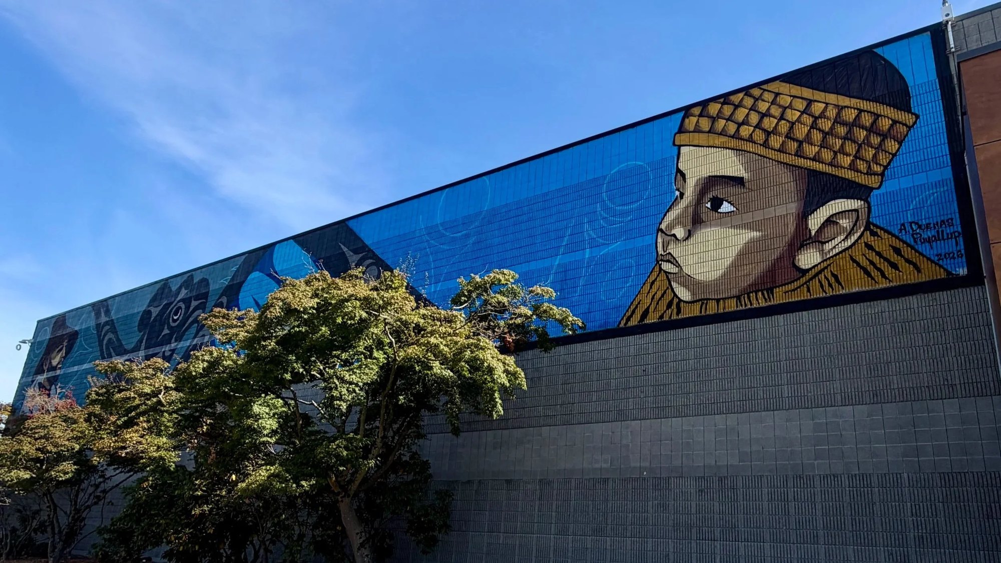 Large colorful mural on a building exterior wall showing a stylized figure in a gold-patterned garment against a blue geometric background.