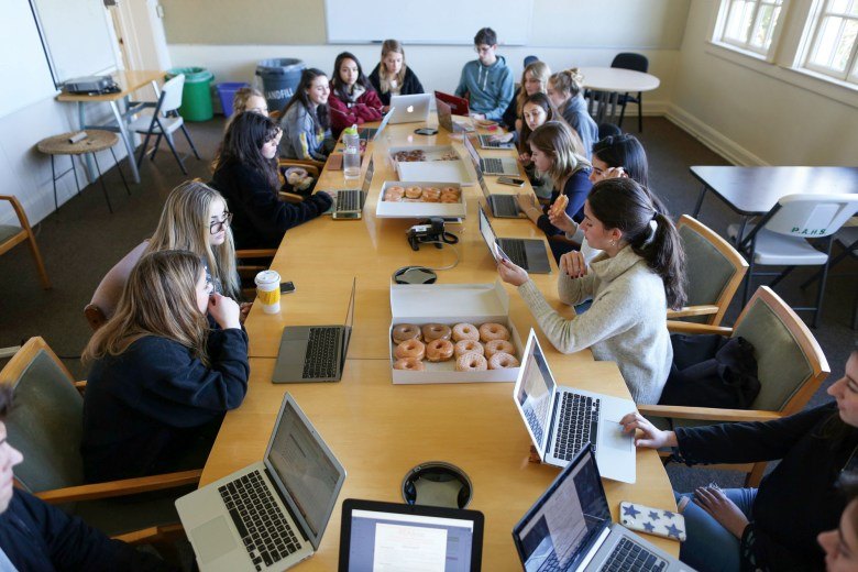 A group of students seated around a conference table with multiple open laptops.