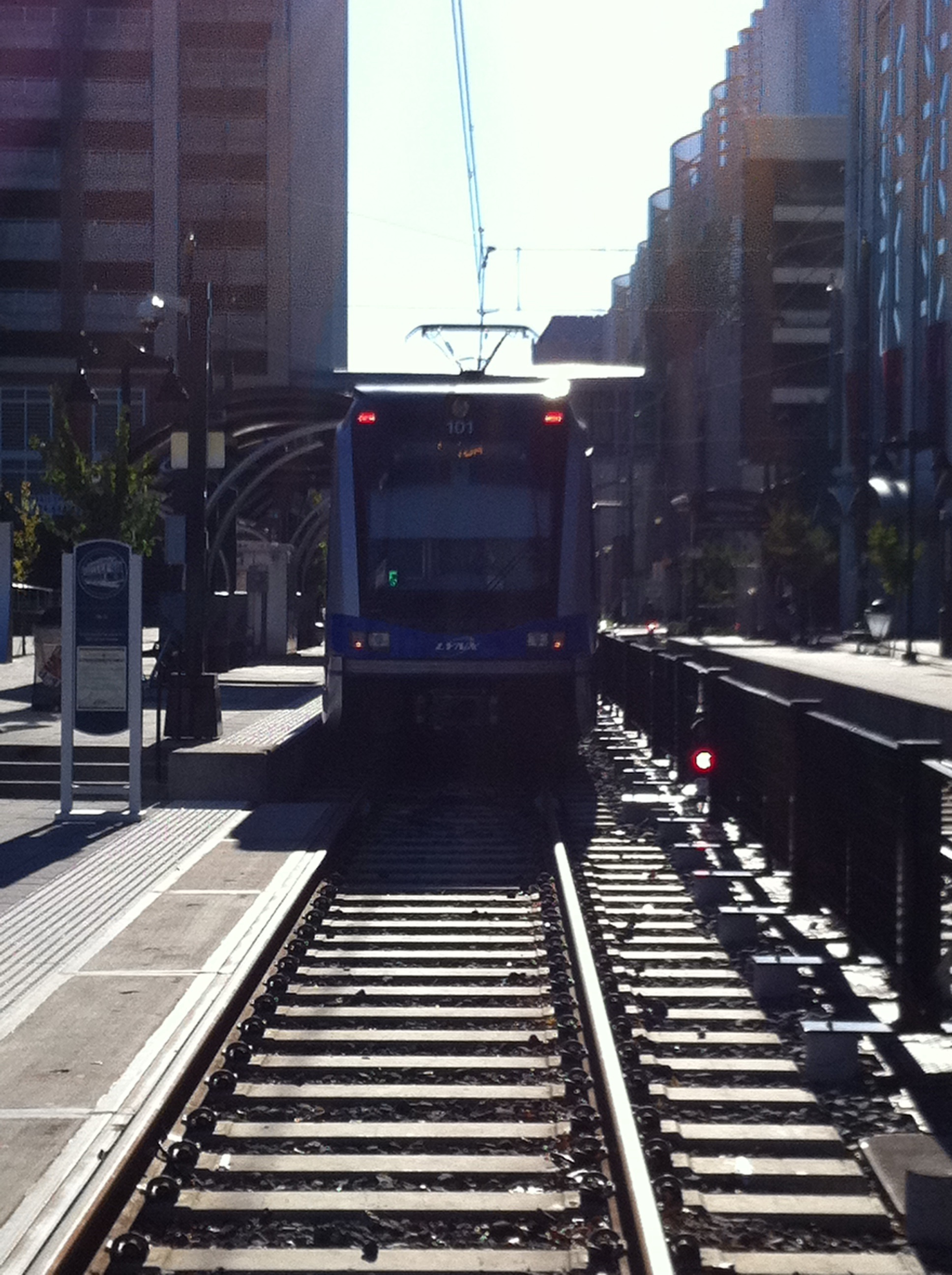 A blue-and-white light rail train stopped at an urban station platform.