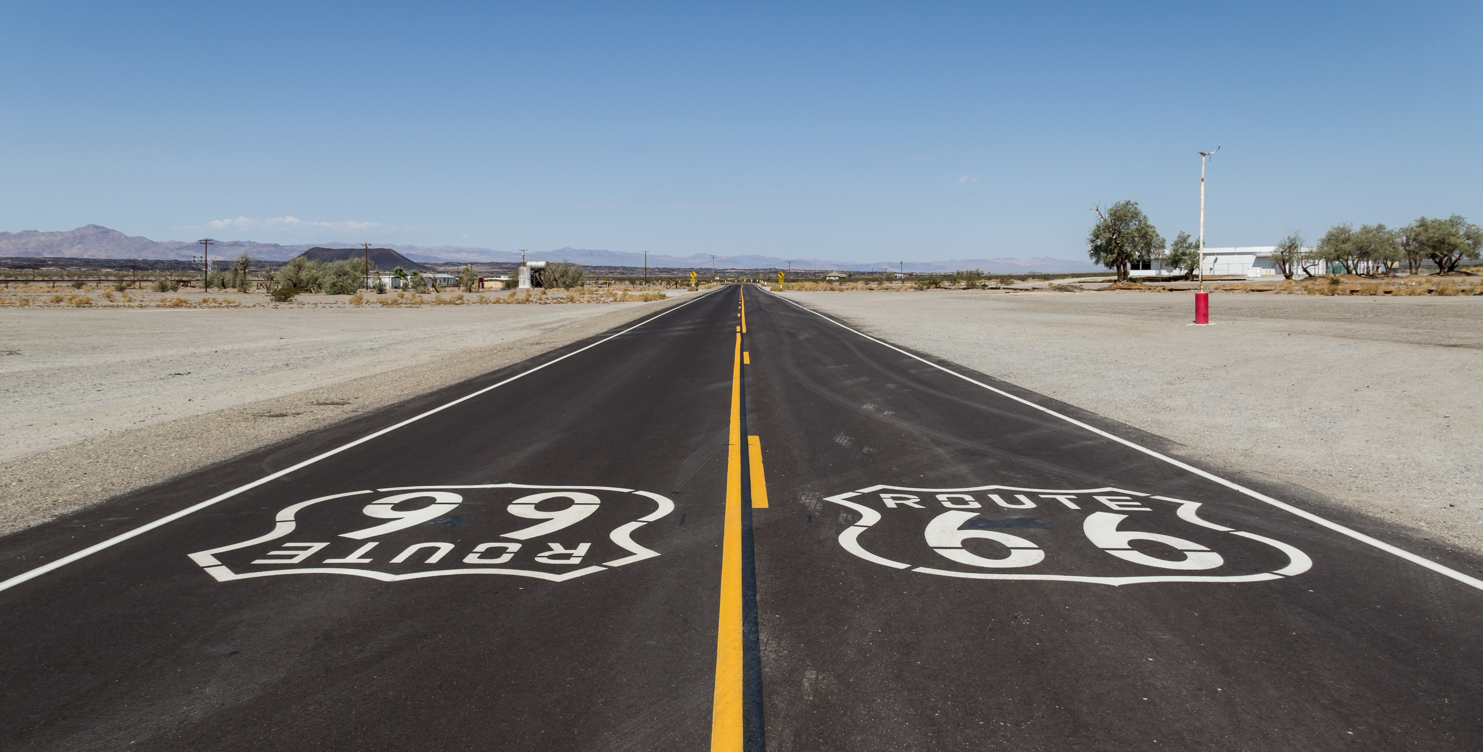 Two-lane desert highway with white Route 66 shield logos painted on the road.