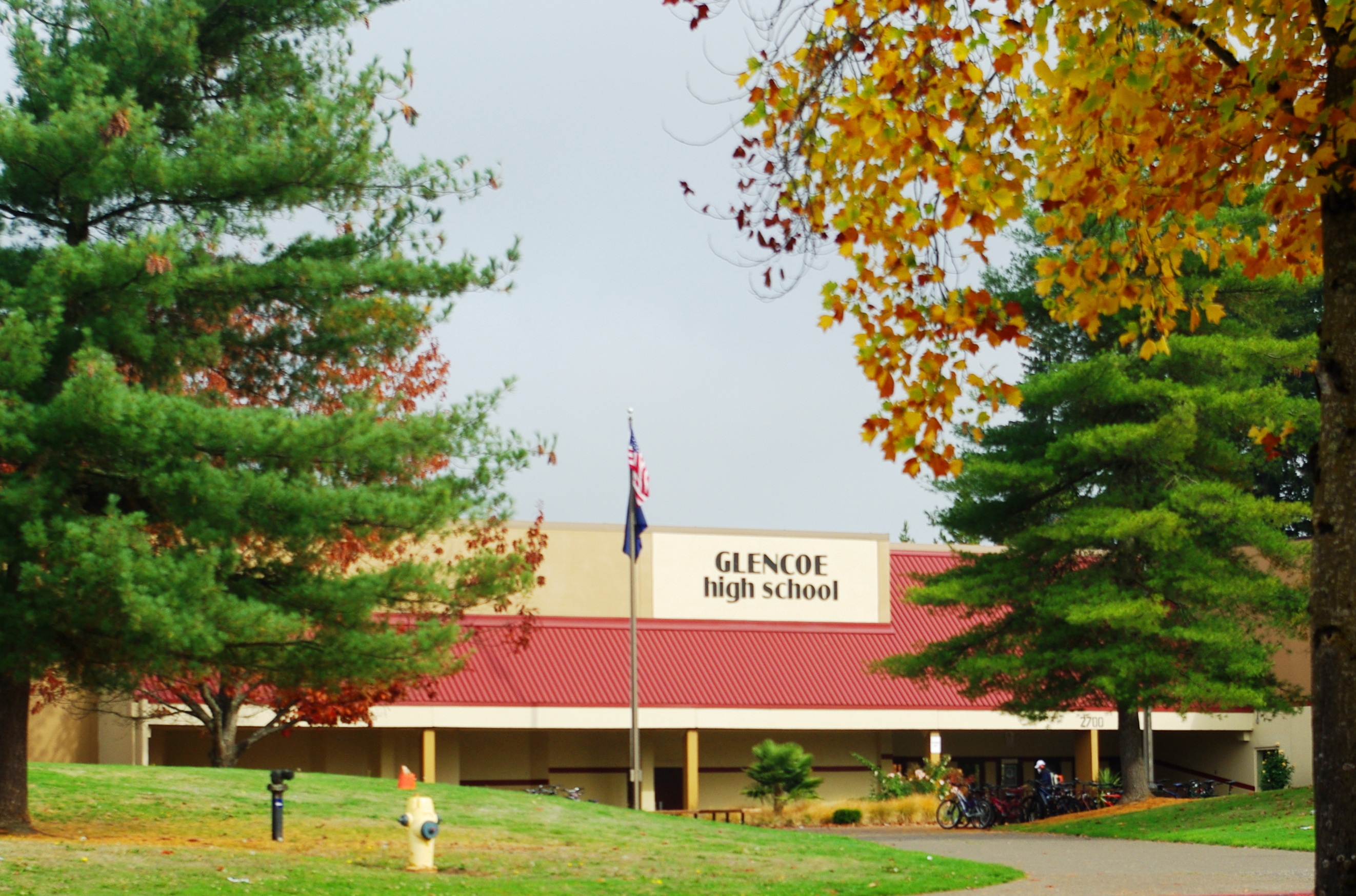 Exterior entrance of a high school with a red roof, school sign, and American flag.