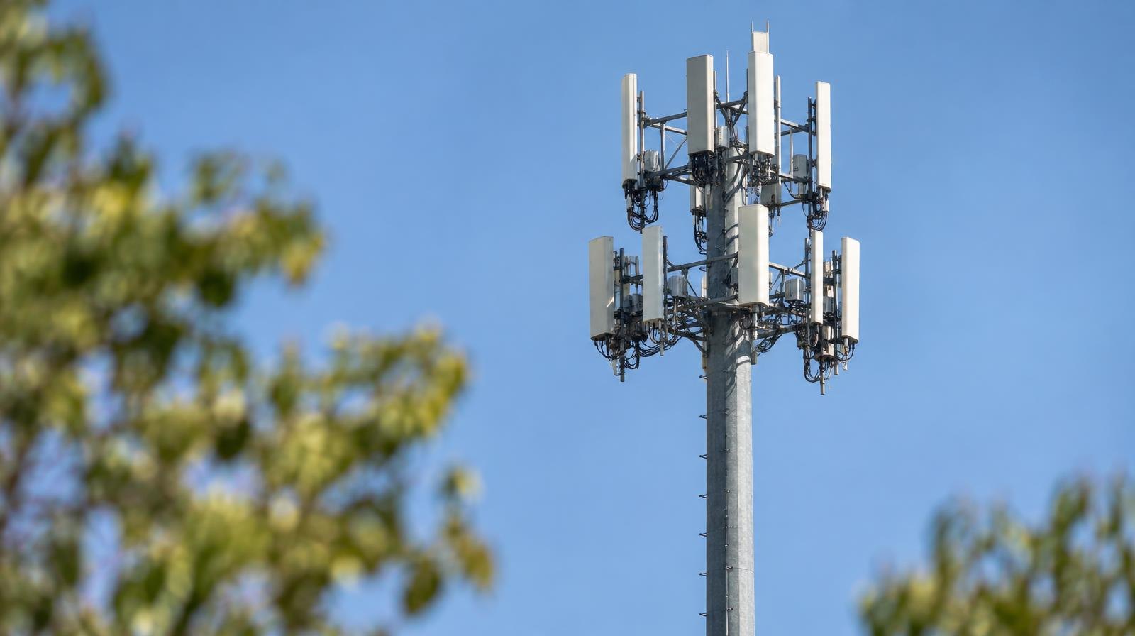 Tall steel cell tower monopole with antenna arrays against a clear blue sky.