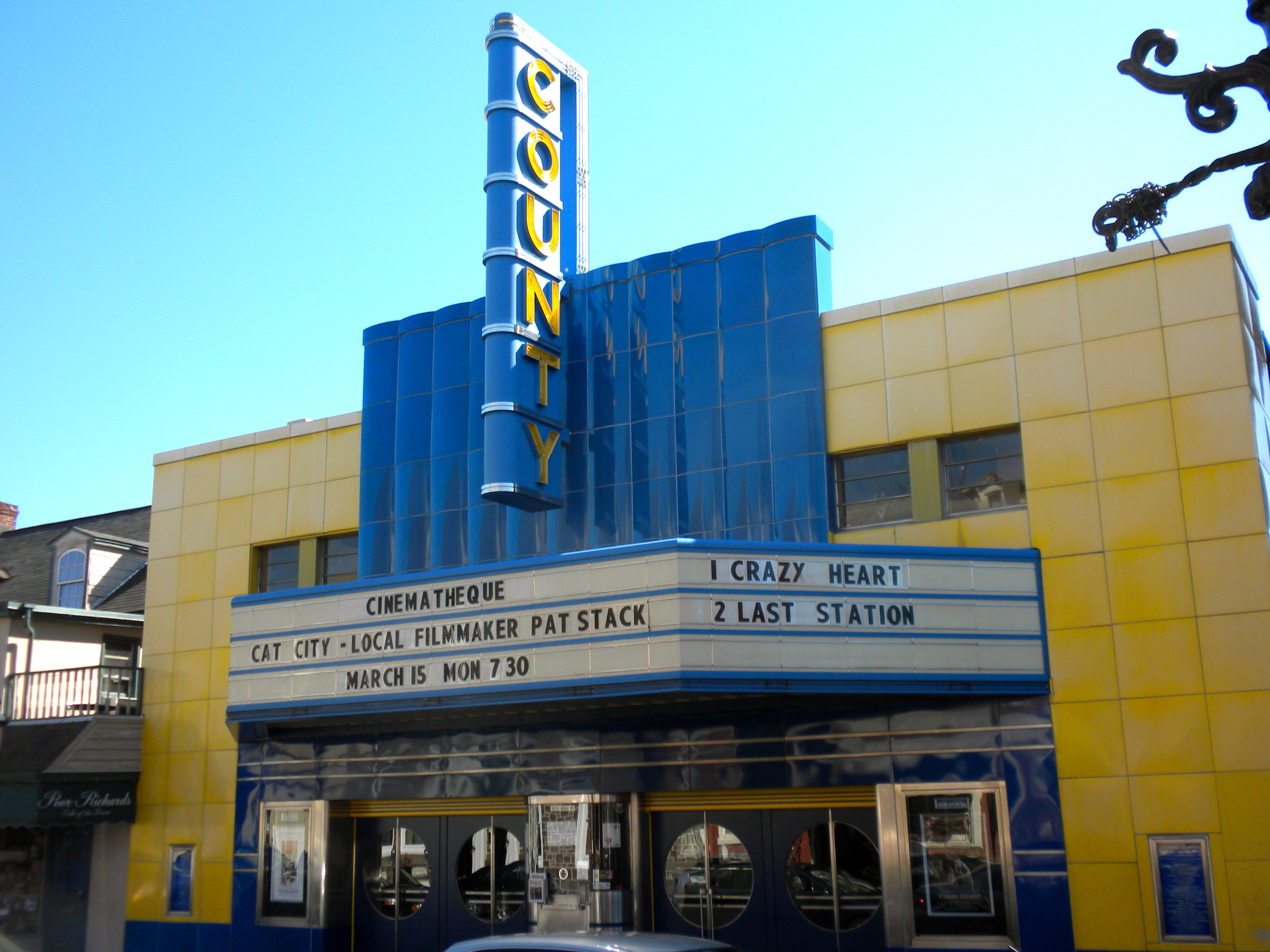 Art Deco movie theater with blue and yellow tile facade and vertical neon sign reading COUNTY.