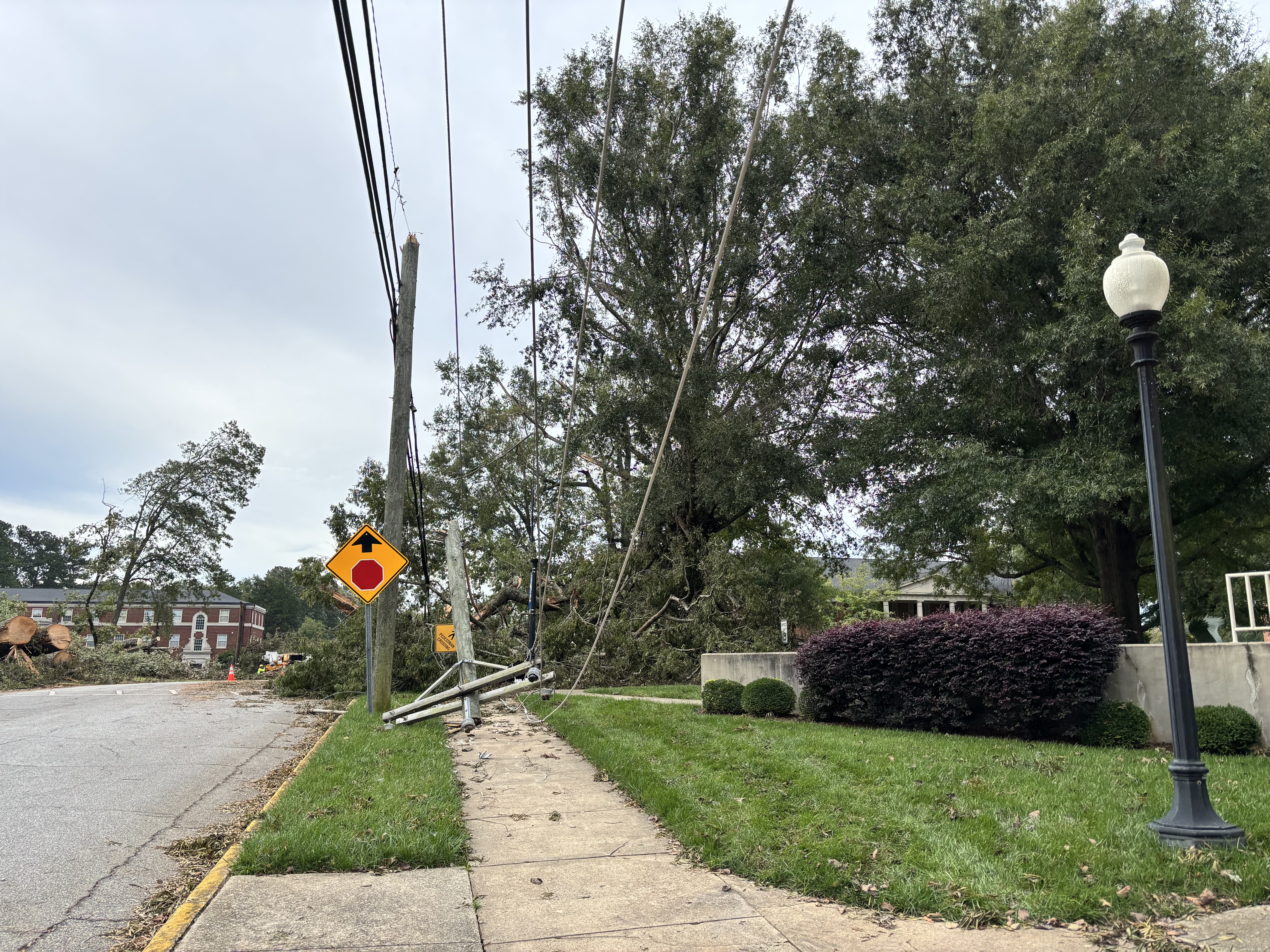 Downed power lines and leaning utility poles along a sidewalk with fallen tree limbs and debris.