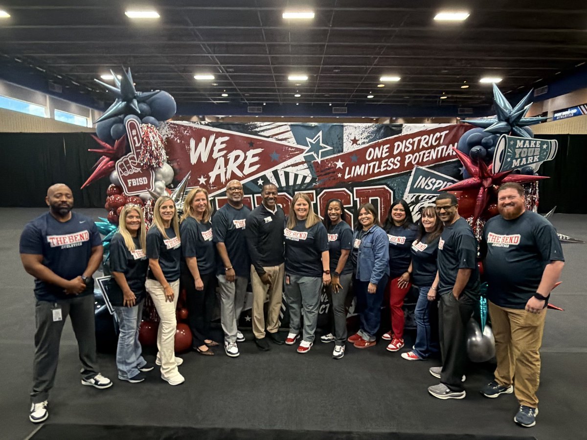 Group of adults in matching navy shirts posing in front of a large motivational banner with star balloons.