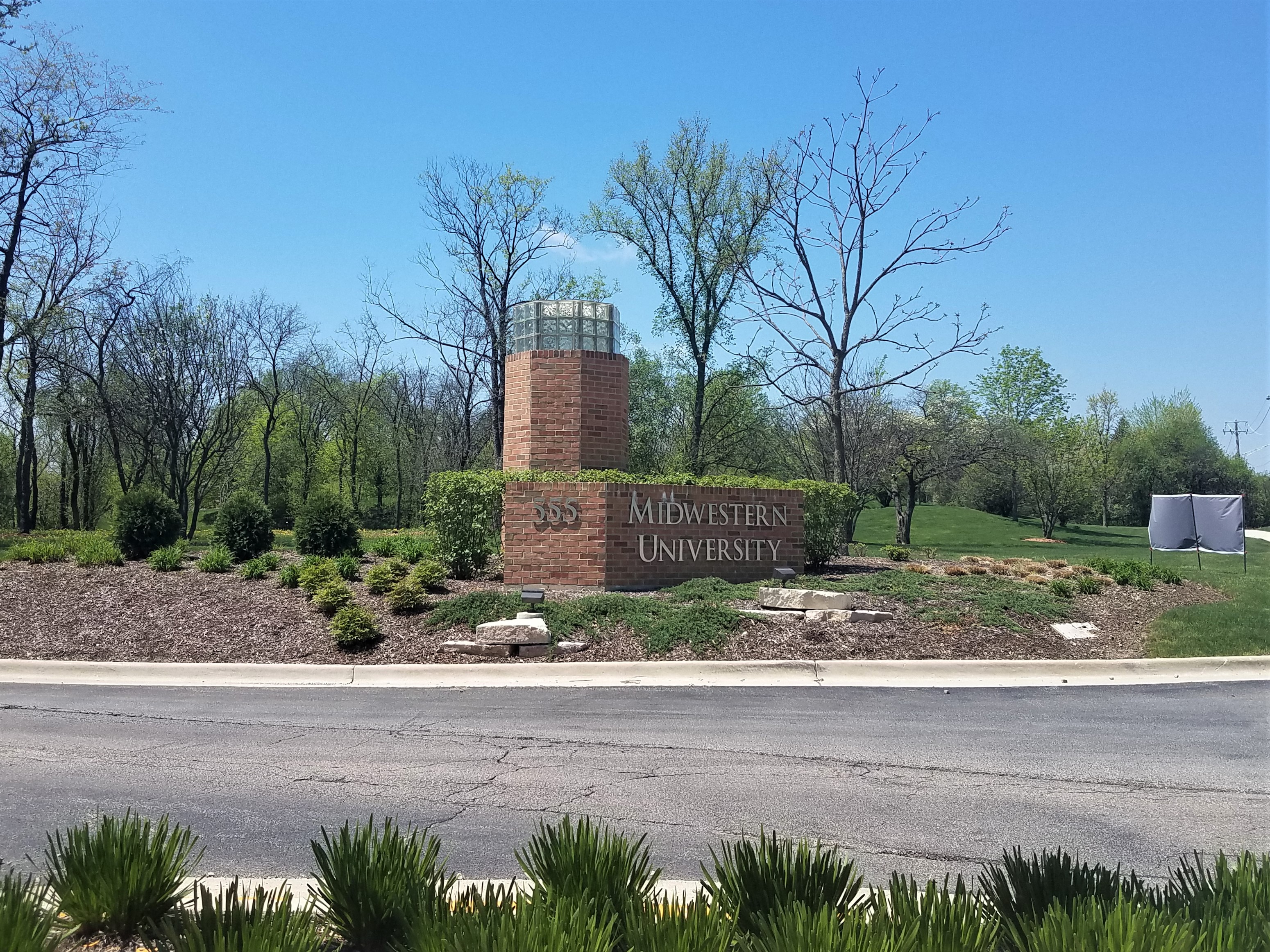 Brick entrance monument sign reading 'Midwestern University' surrounded by landscaping and trees.