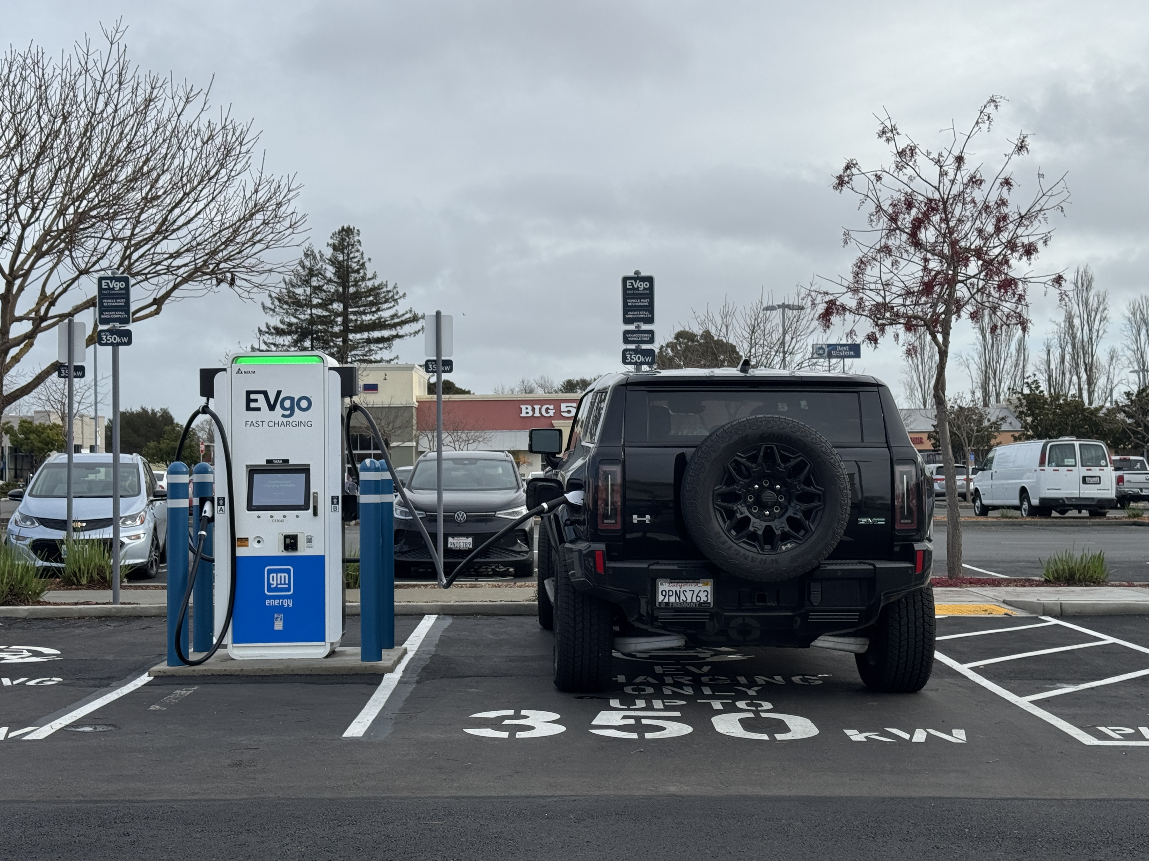 A black electric SUV plugged into a fast-charging station in a parking lot.