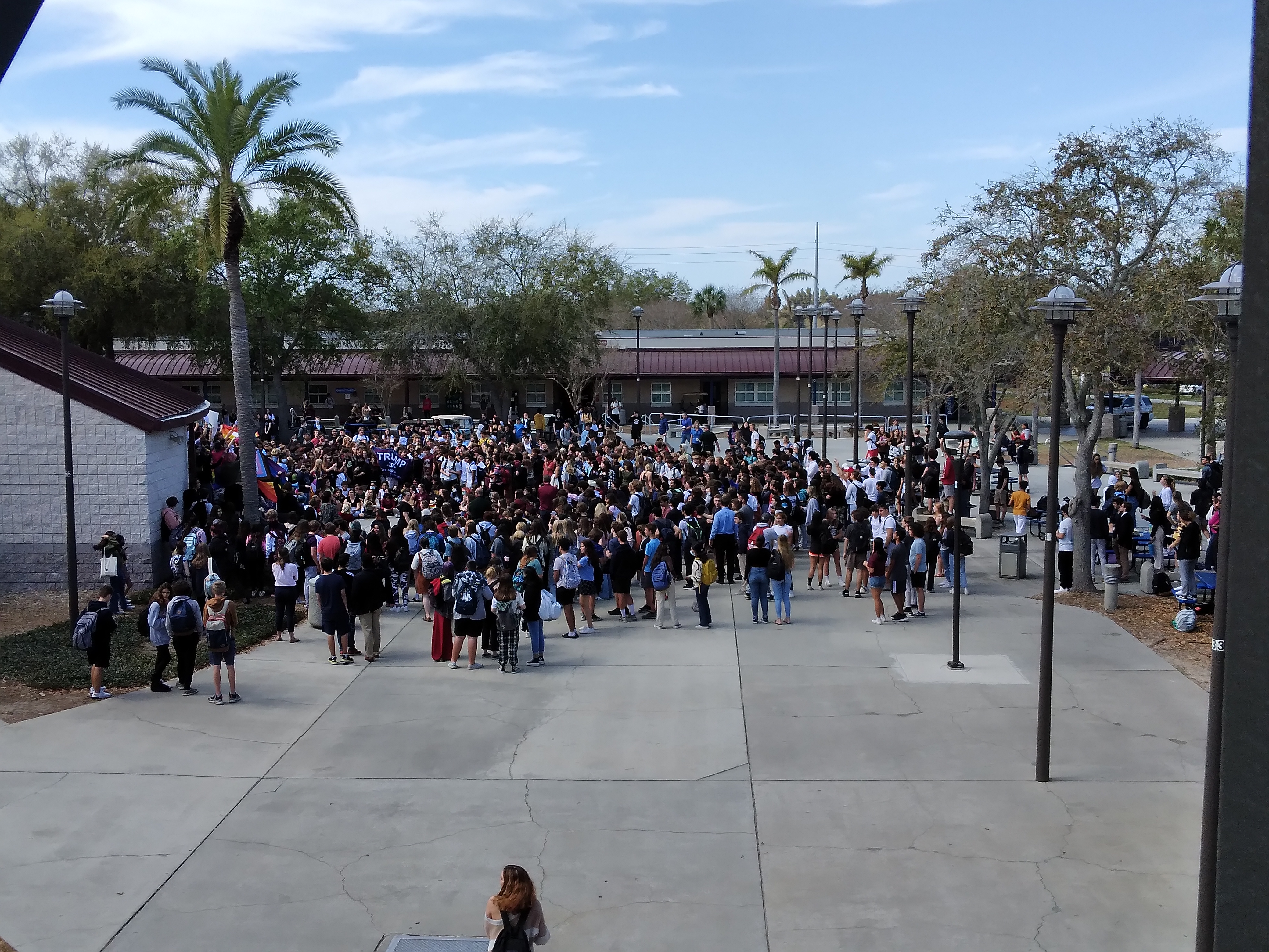 Large crowd of students assembled in an outdoor school courtyard with palm trees in the background.