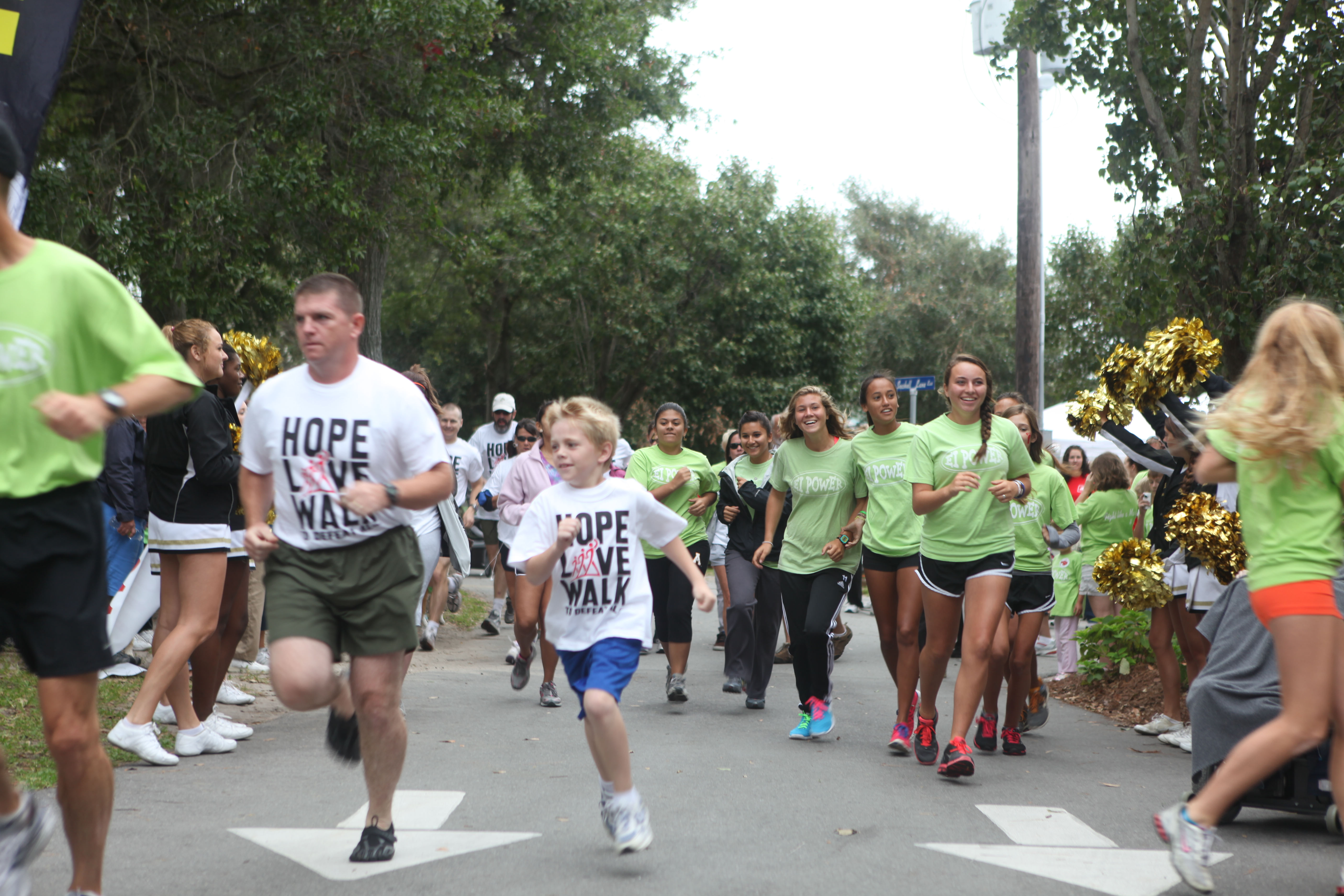 A crowd of adults and children walking along a road at a charity fundraiser event.