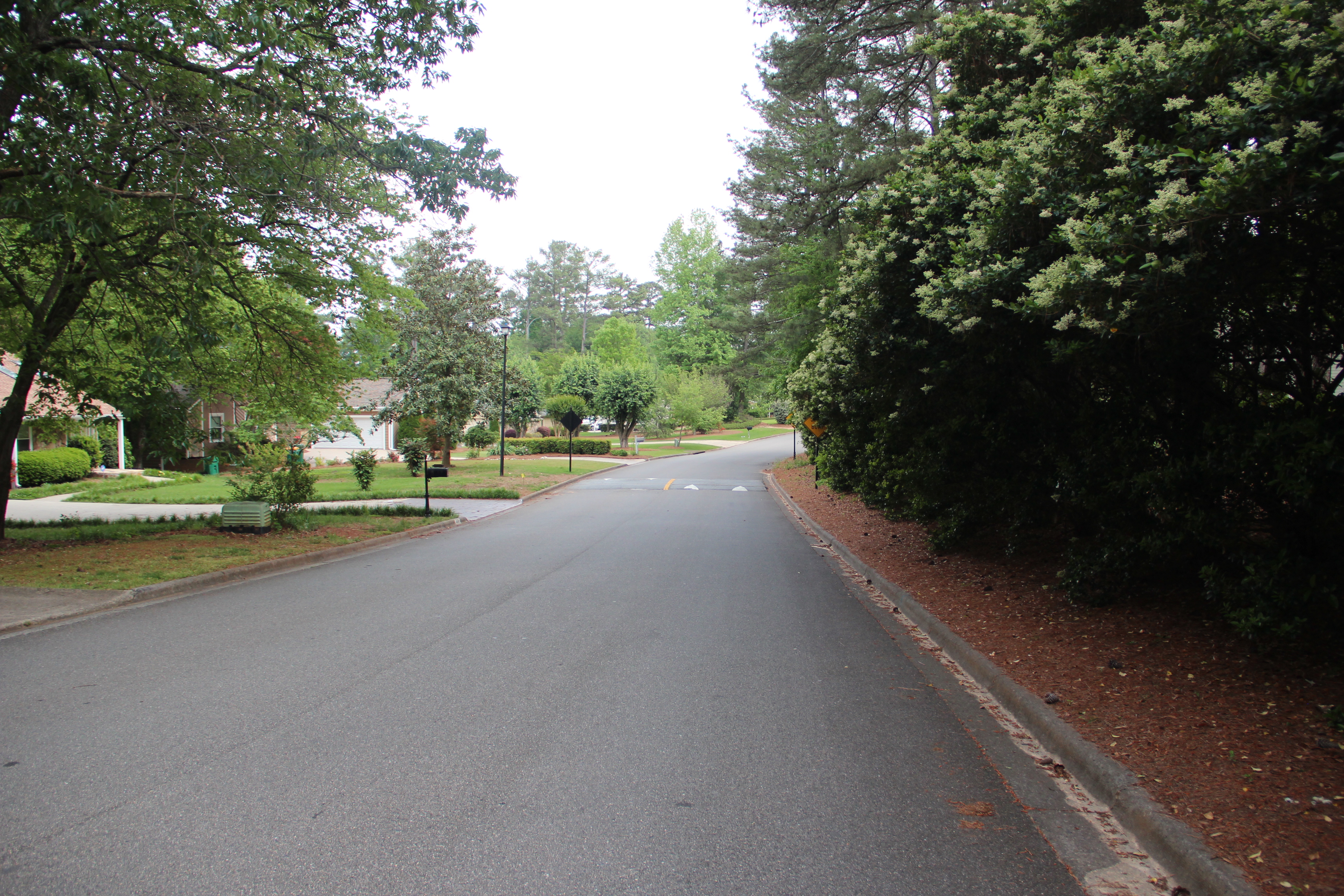 A paved residential road in Johns Creek, Georgia under a clear sky.
