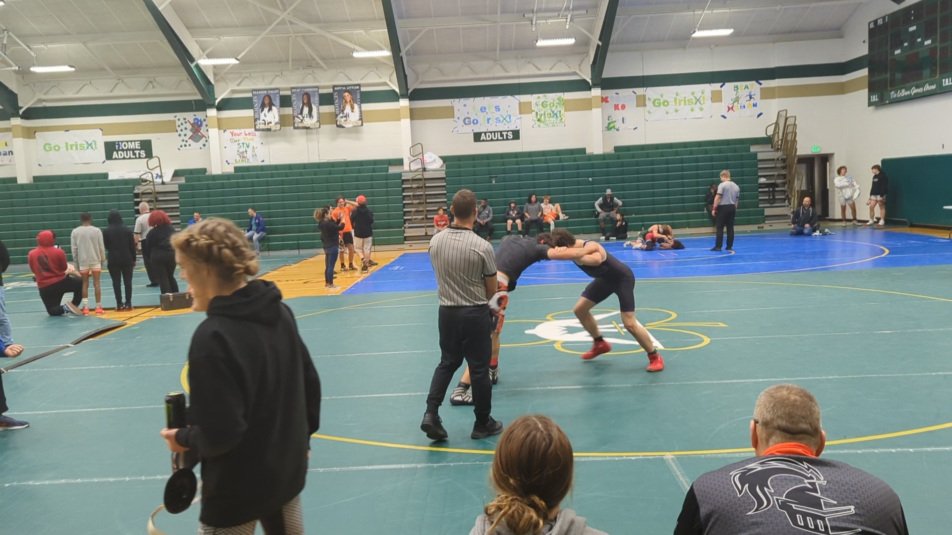 High school wrestlers compete on mats in a gymnasium while referees and spectators watch.