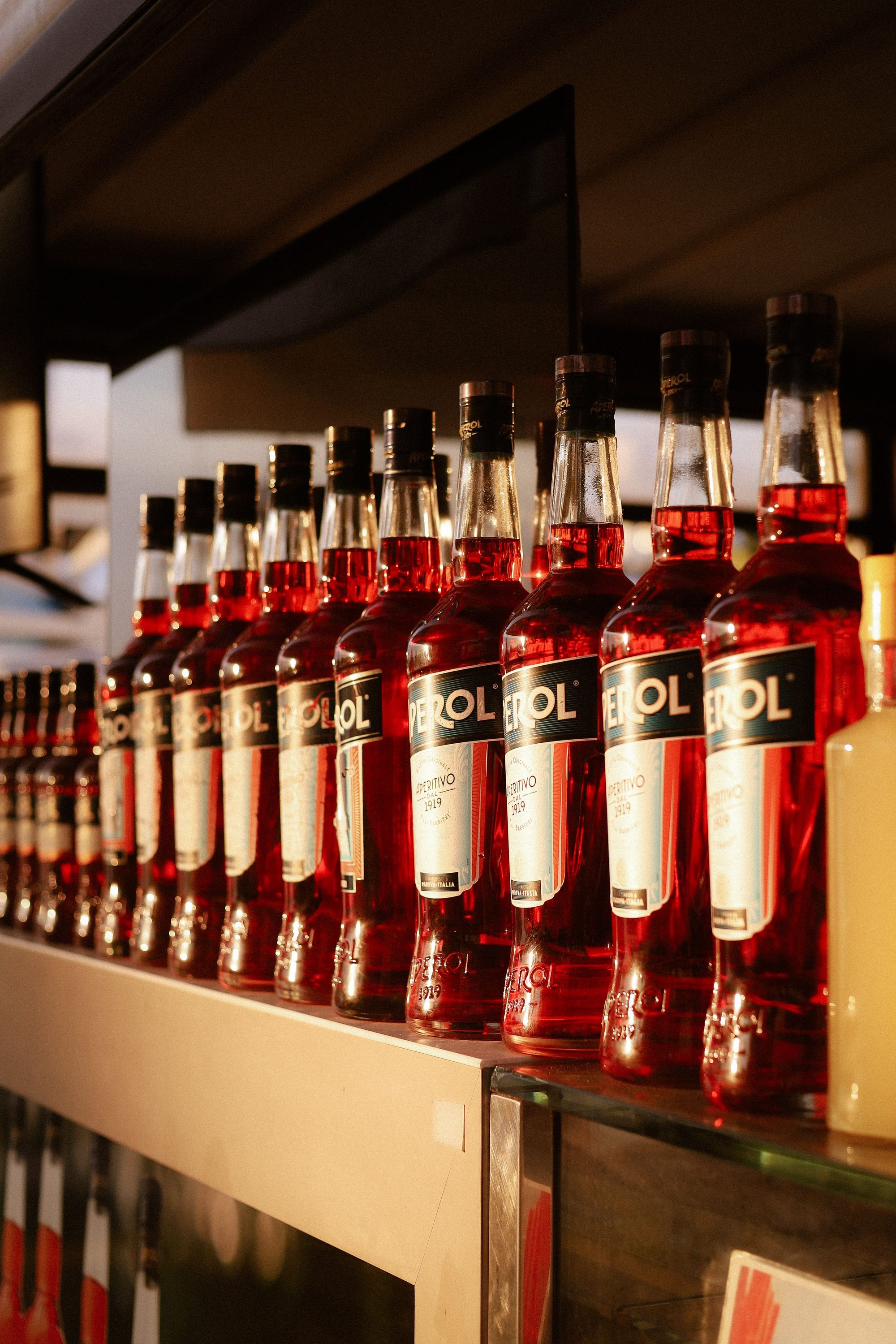 A series of Aperol bottles beautifully lined up on a bar shelf in Italy during sunset.