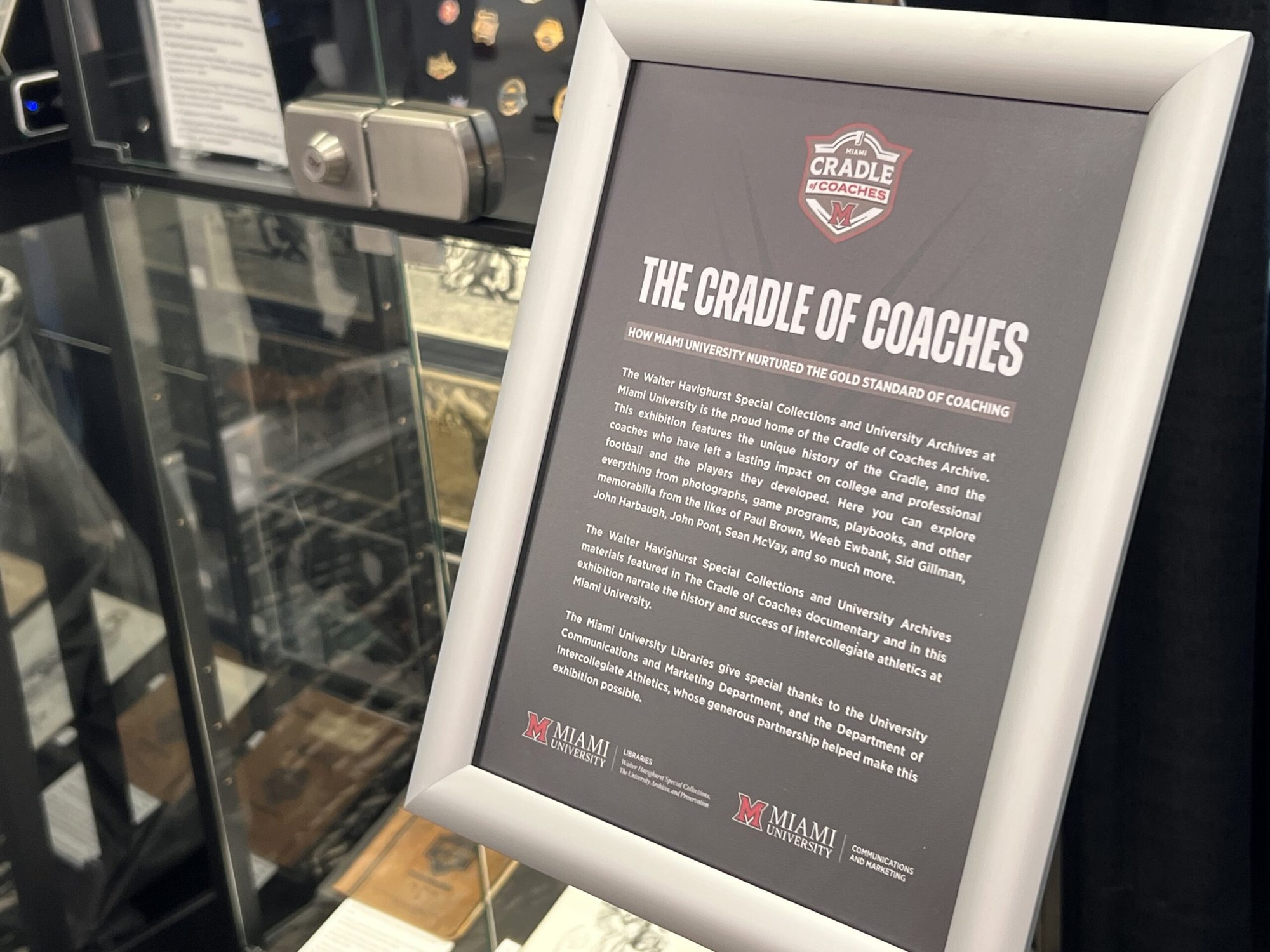 Framed exhibit sign reading 'The Cradle of Coaches' with a university logo on a dark background.