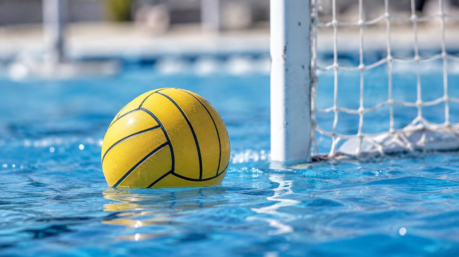 A water polo ball floating on the surface of a bright blue pool near a white goal net.