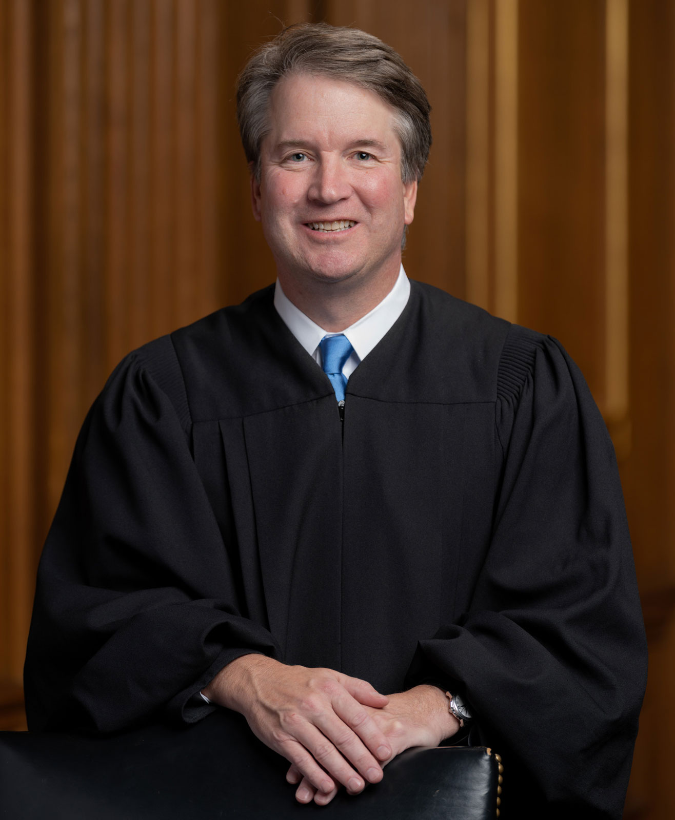 Man in black judicial robe seated with hands folded in a formal portrait.