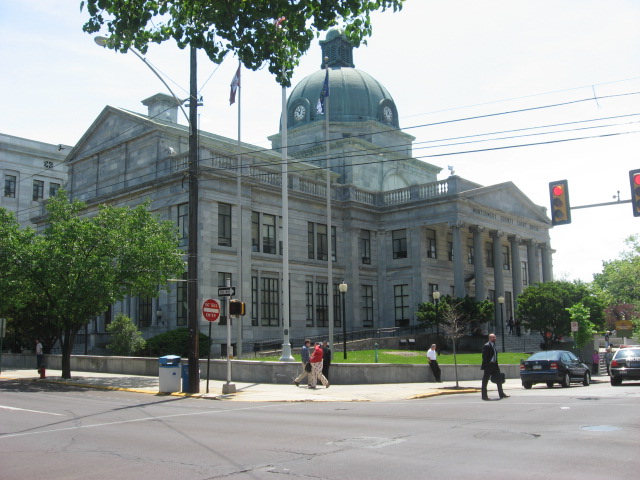 Neoclassical stone courthouse with green copper dome at a street intersection.