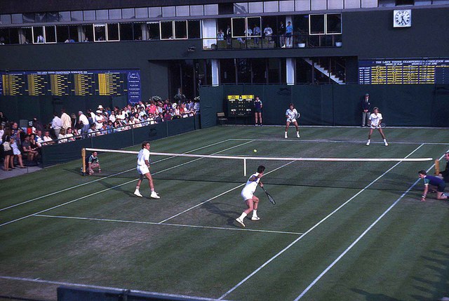 Four tennis players compete in a doubles match on an outdoor court.