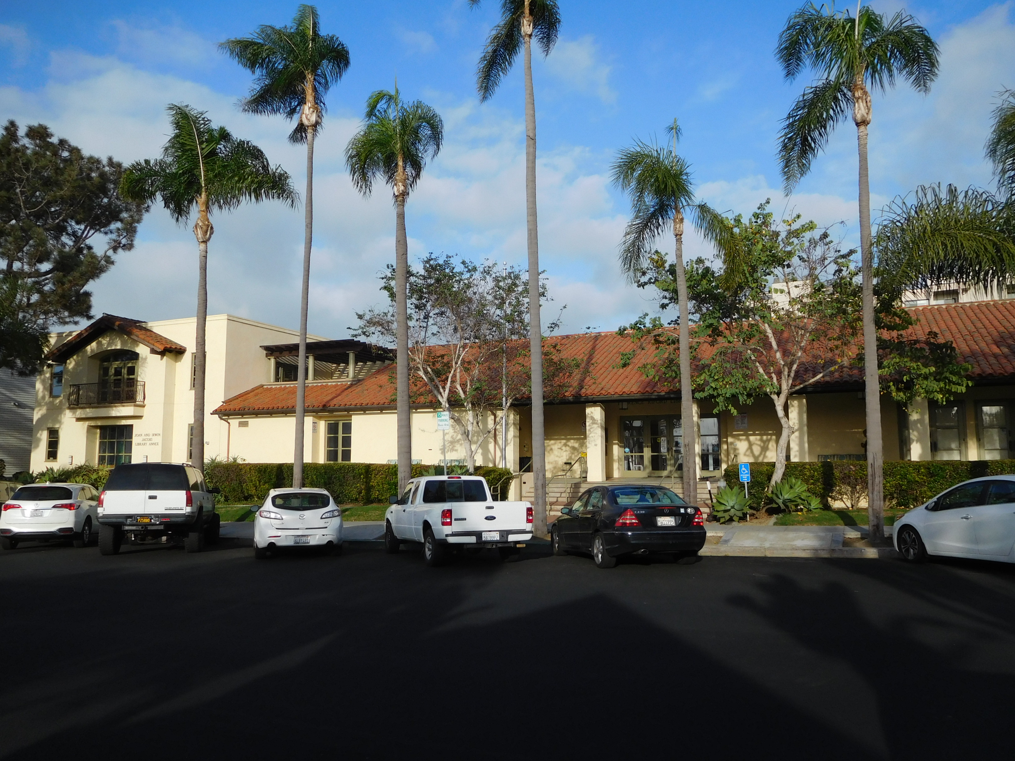 Spanish-style library building with a red tile roof and tall royal palm trees in front.