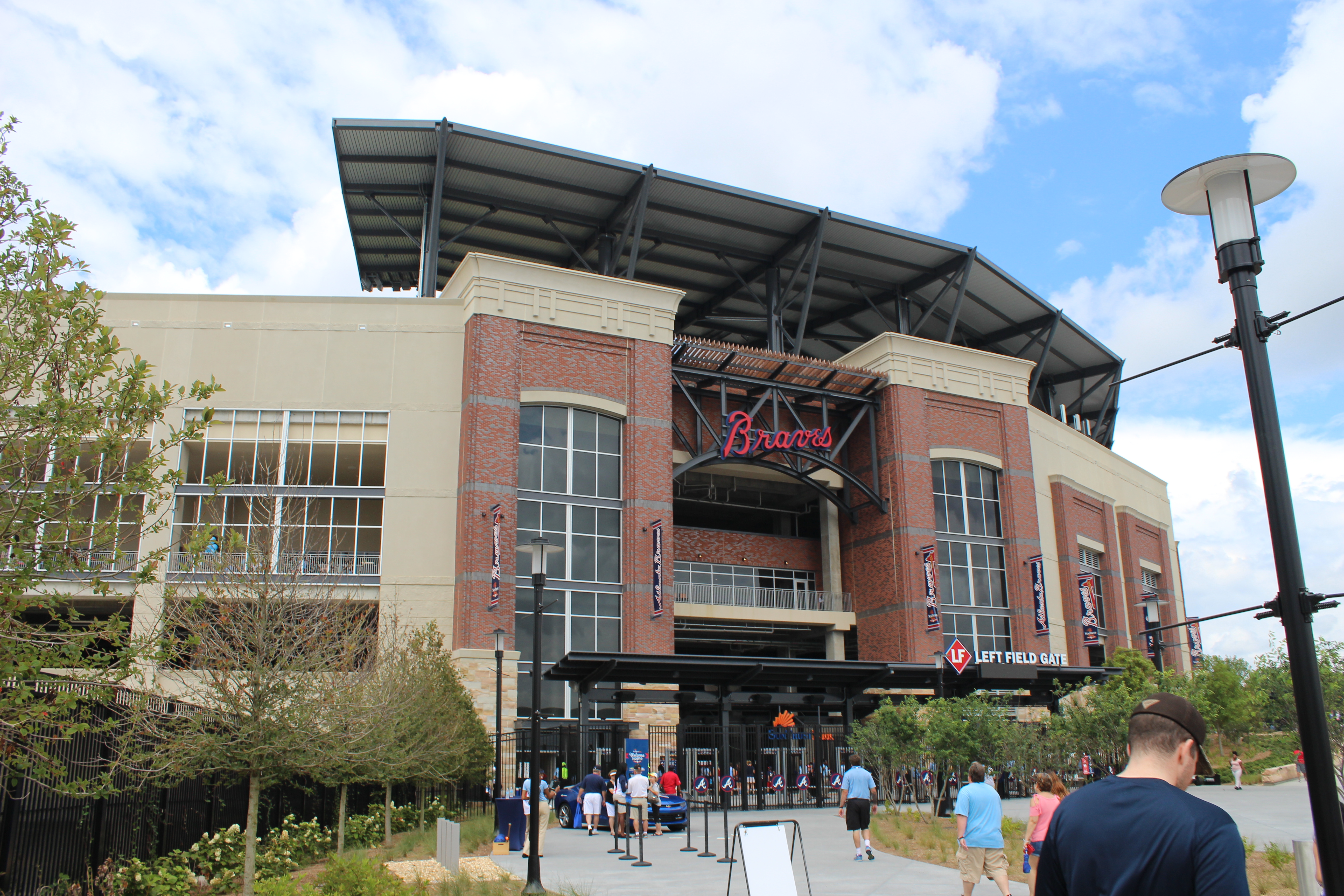 Exterior of a baseball stadium with a brick facade and fans walking toward the entrance gate.