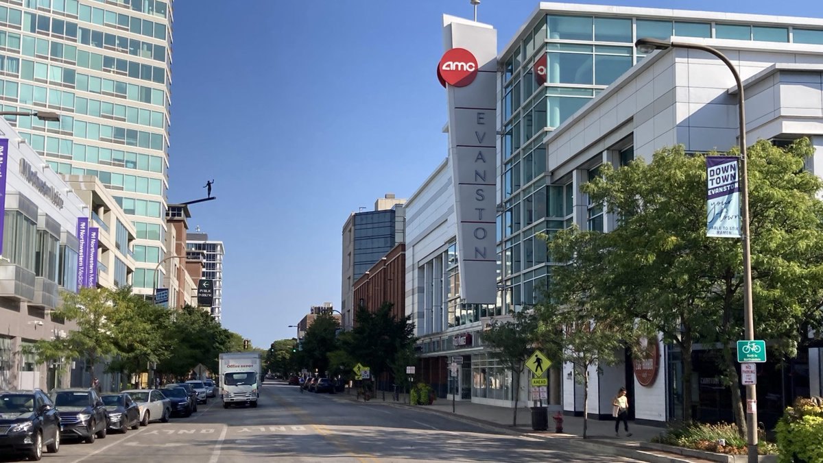 Street-level view of the AMC Evanston theater with its red circular logo and vertical sign on a mixed-use building.