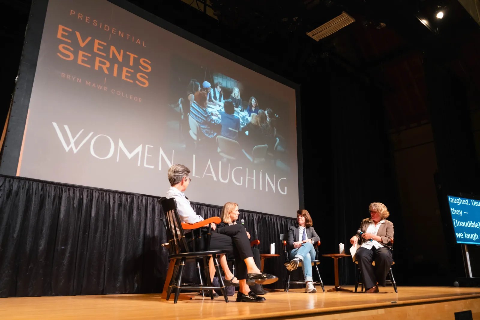 Four panelists seated on a stage with a projected screen reading 'Women Laughing' behind them.