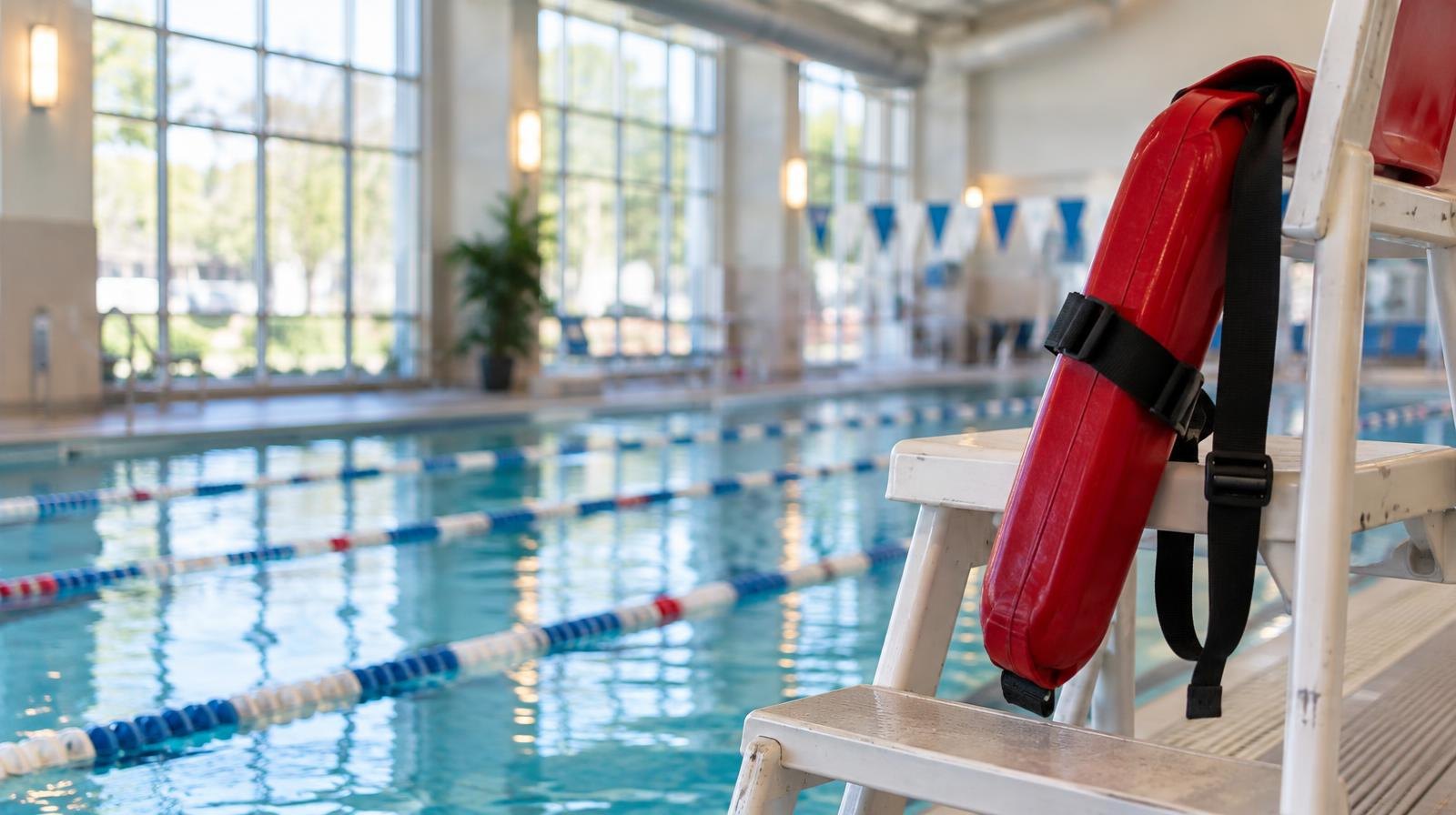 Bright indoor pool with colorful lane markers, a lifeguard chair, and sunlight through large windows.