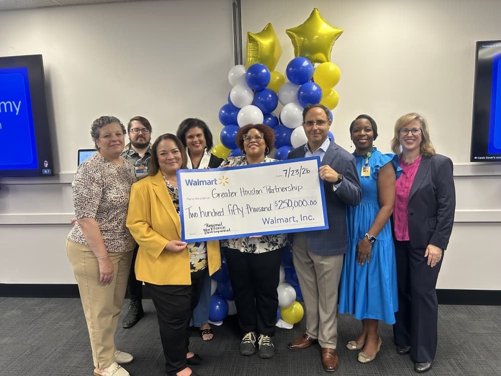 Group of eight people holding a large ceremonial check for $250,000 indoors with balloons.