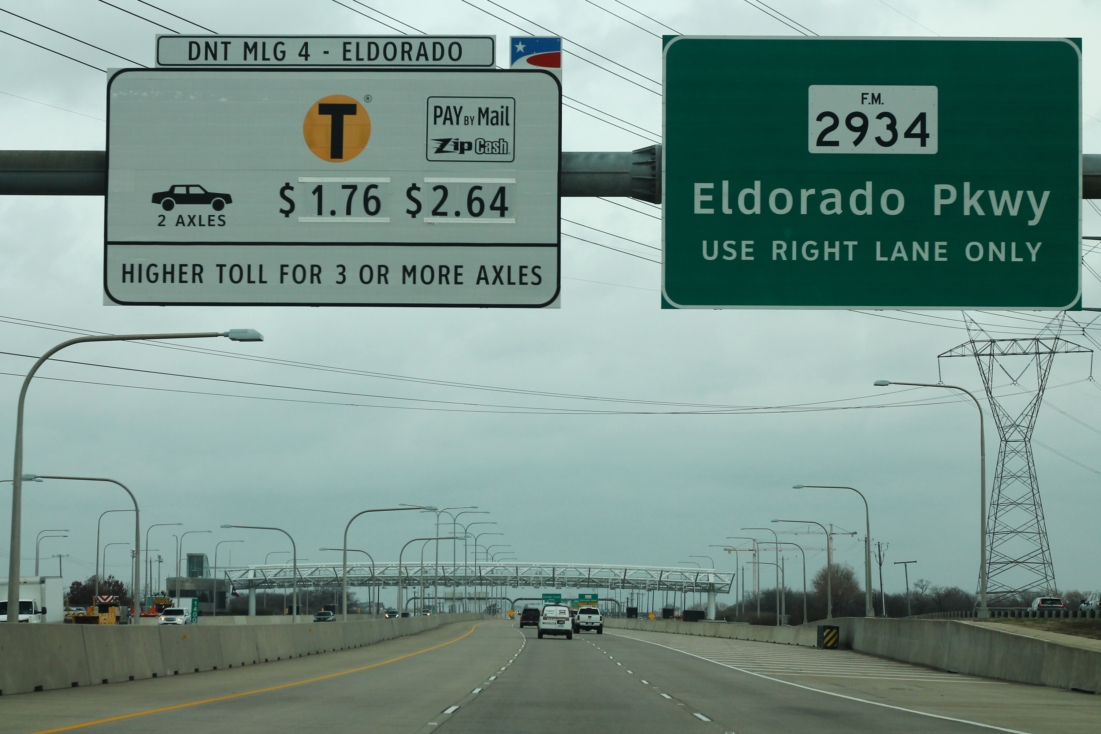 Overhead toll signs on the Dallas North Tollway at a highway interchange.