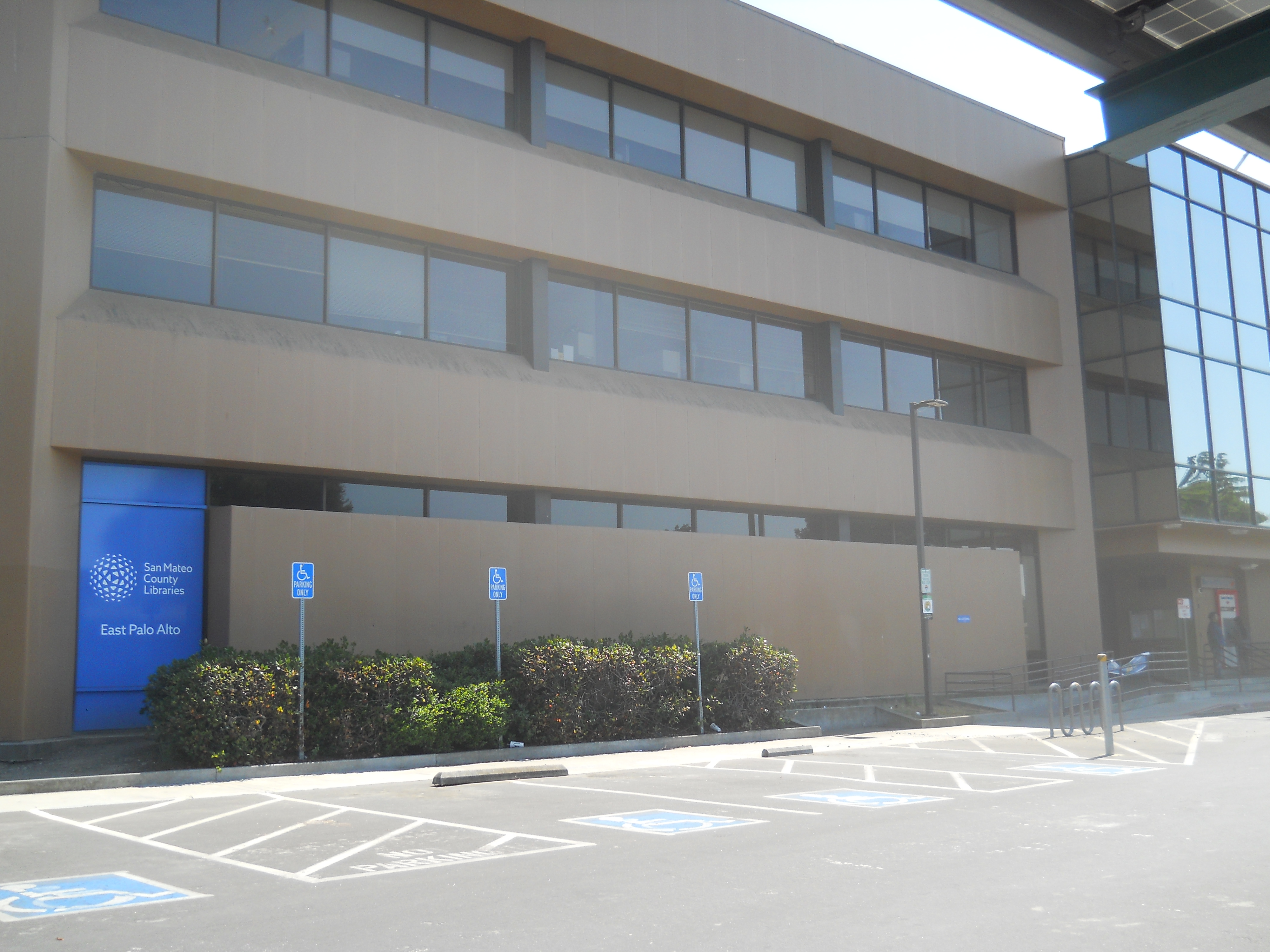 Two-story tan municipal building with a blue entrance door and library signage.