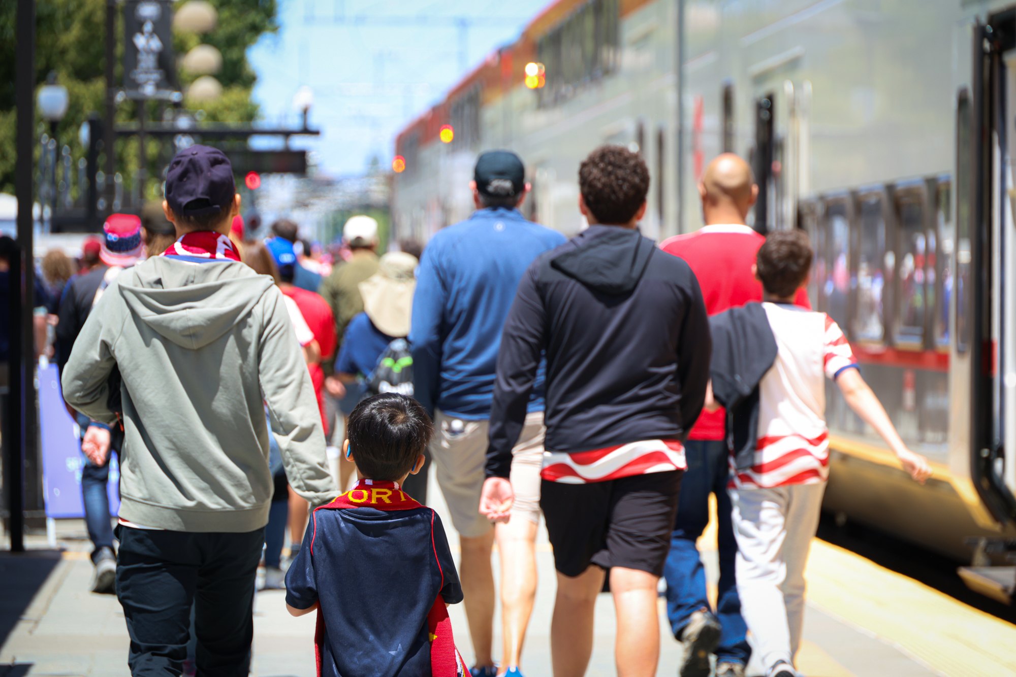 A group of adults and children walking alongside a silver Caltrain passenger car at a station platform.