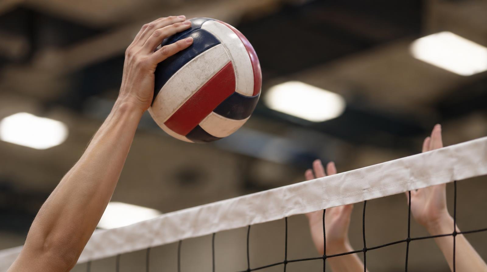 A volleyball being spiked over a net inside a gymnasium.