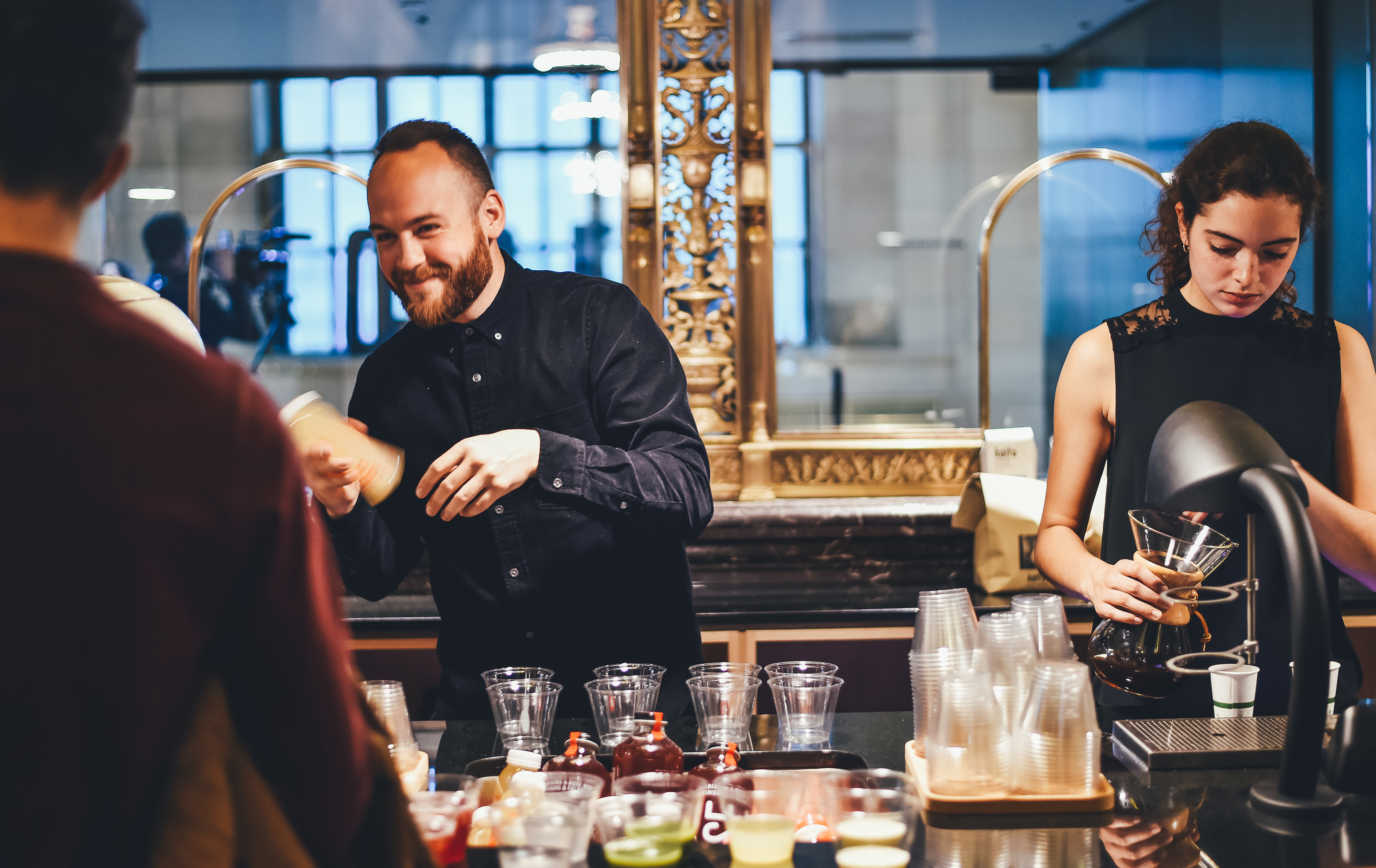 Two bartenders smile and work behind a bar stocked with glasses and bottles.
