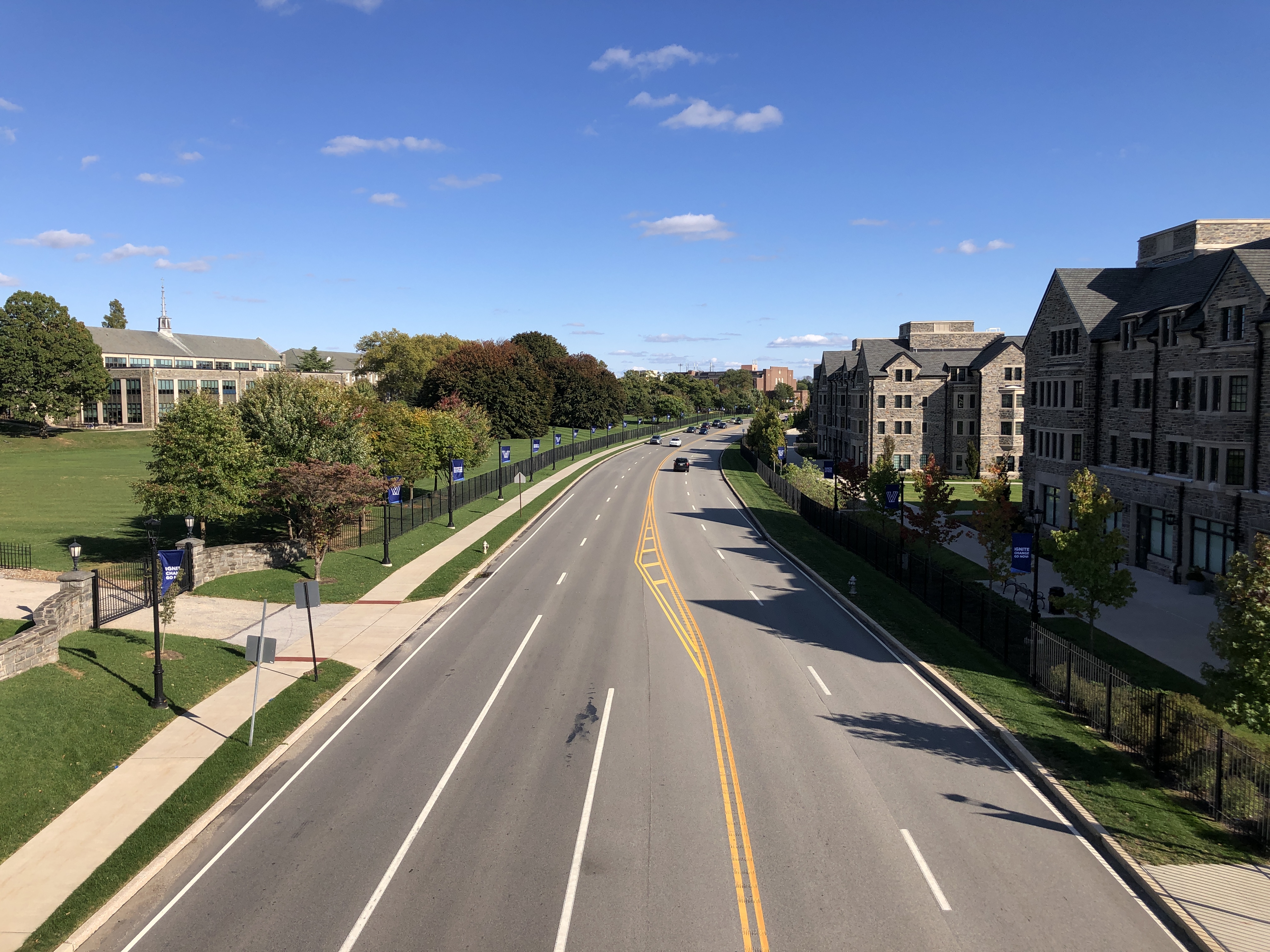 Gothic stone university buildings and green lawns along a wide road on a sunny day.