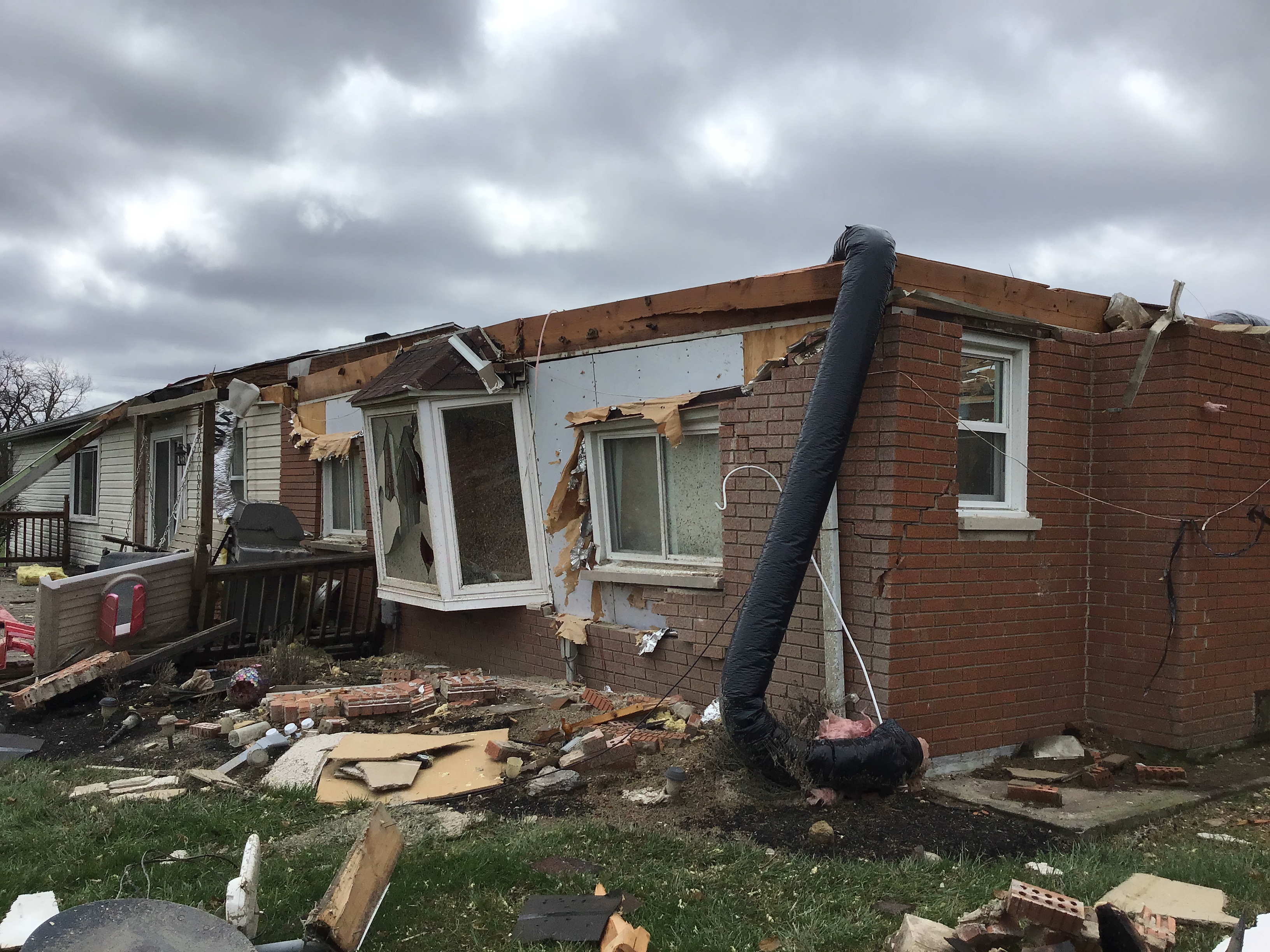 Brick ranch home with roof torn off and debris scattered across the yard after a tornado.