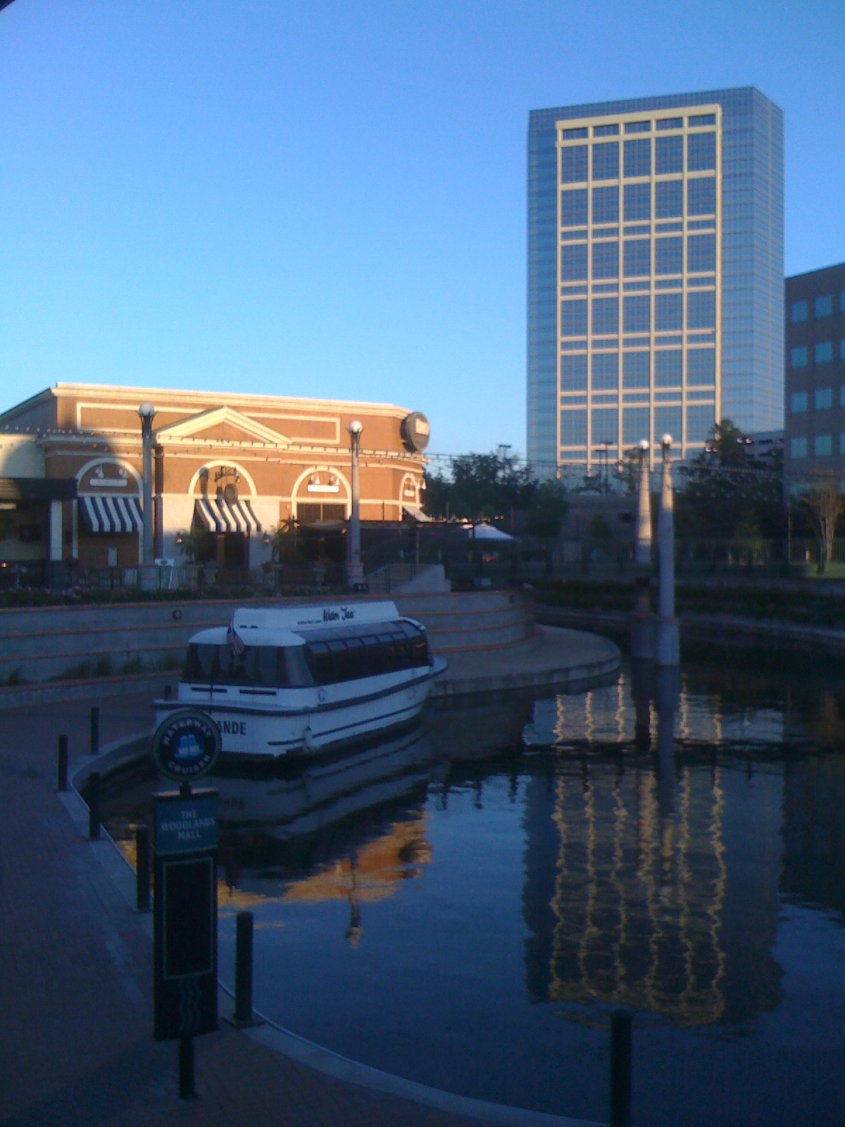 A calm urban waterway with a docked white boat and glass office tower reflected in the water.