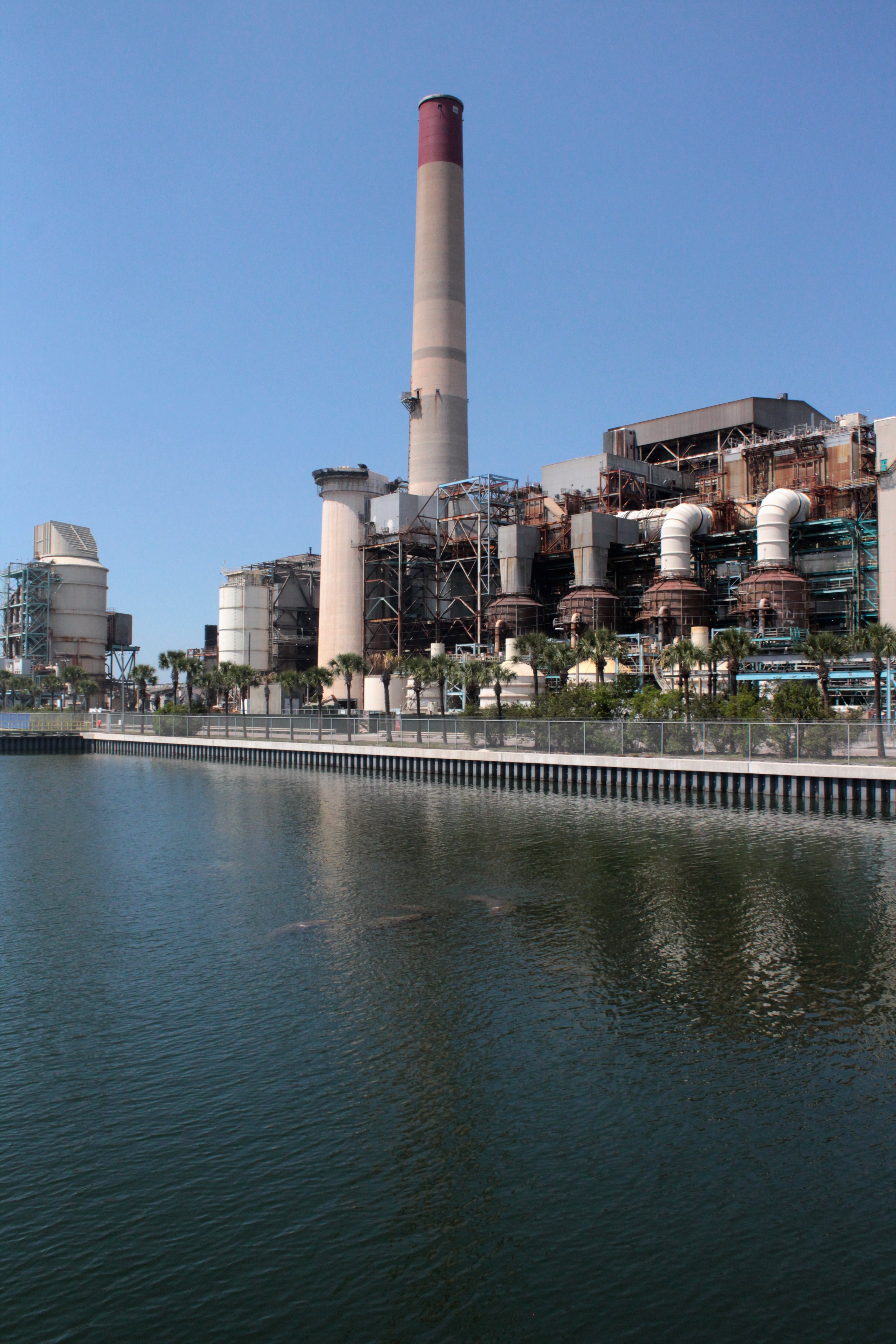 Industrial power station with a tall red-and-white smokestack beside a calm waterway