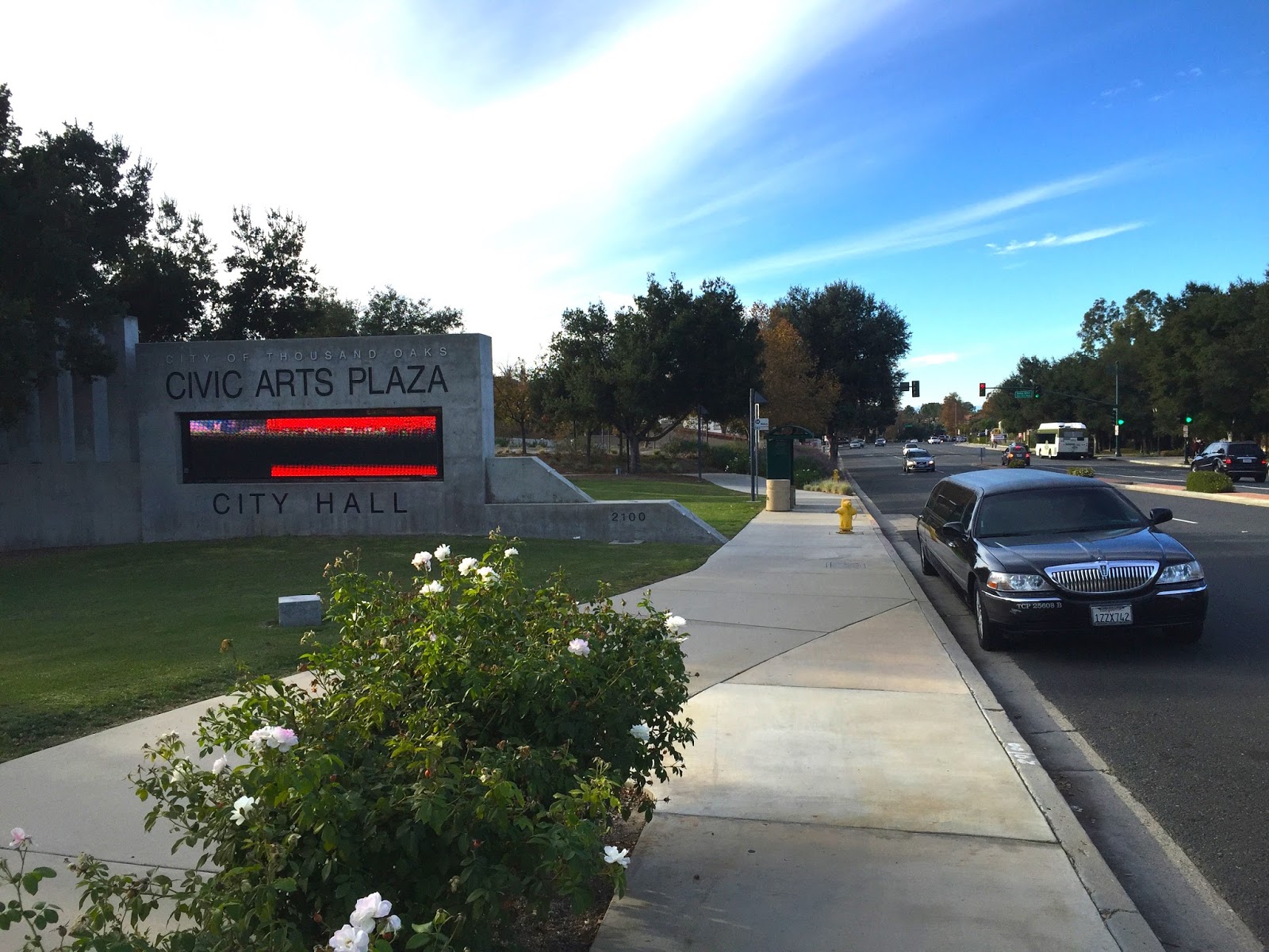Monument sign for Civic Arts Plaza and City Hall beside a tree-lined street.